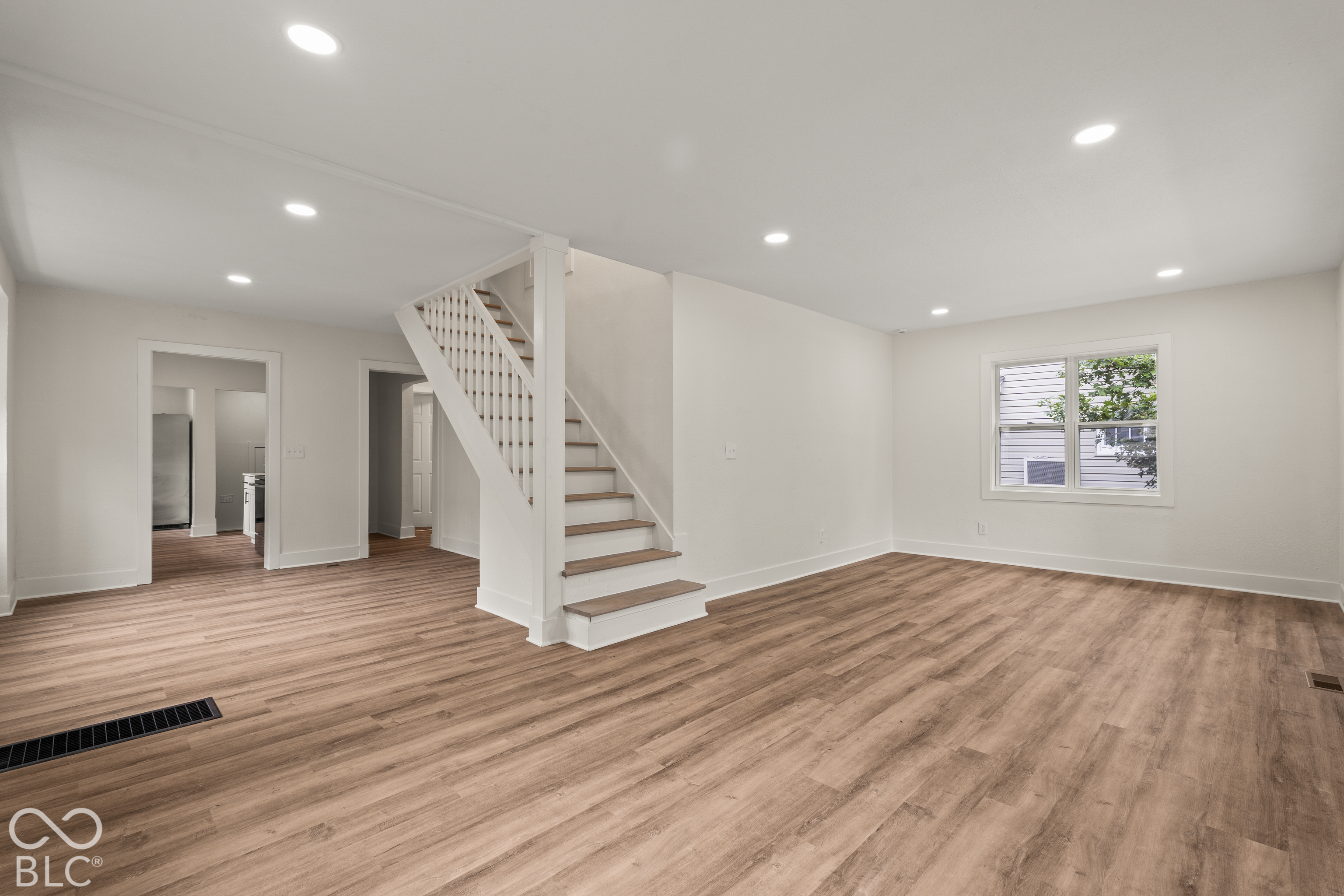 Open-concept interior featuring wood-finish flooring, recessed lighting, and a staircase with white balusters and wood-tone treads Open-concept interior featuring wood-finish flooring, recessed lighting, and a staircase with white balusters and wood-tone treads