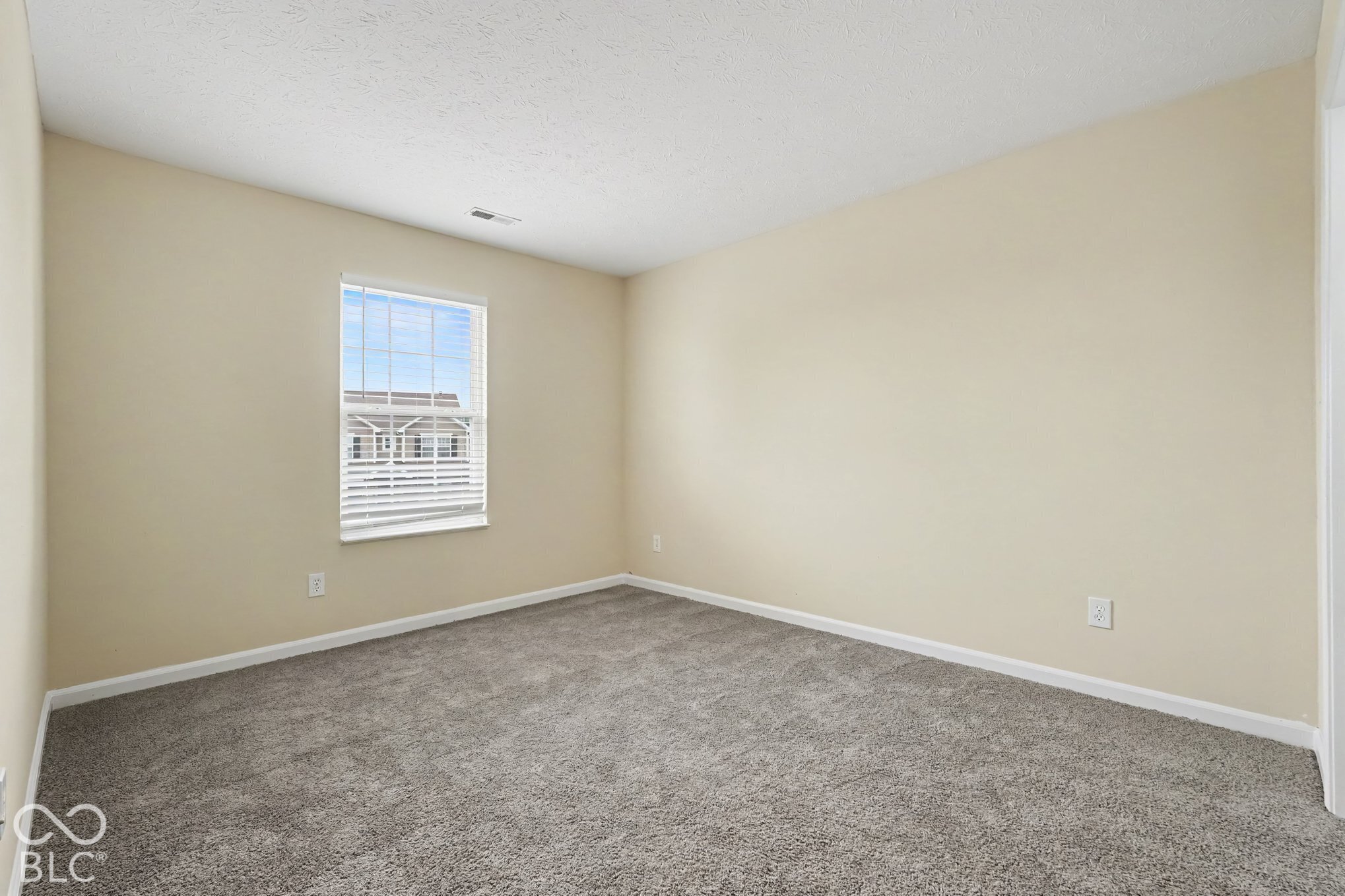 Neutral-toned walls, wall-to-wall carpeting, and a double-hung window with fitted blinds