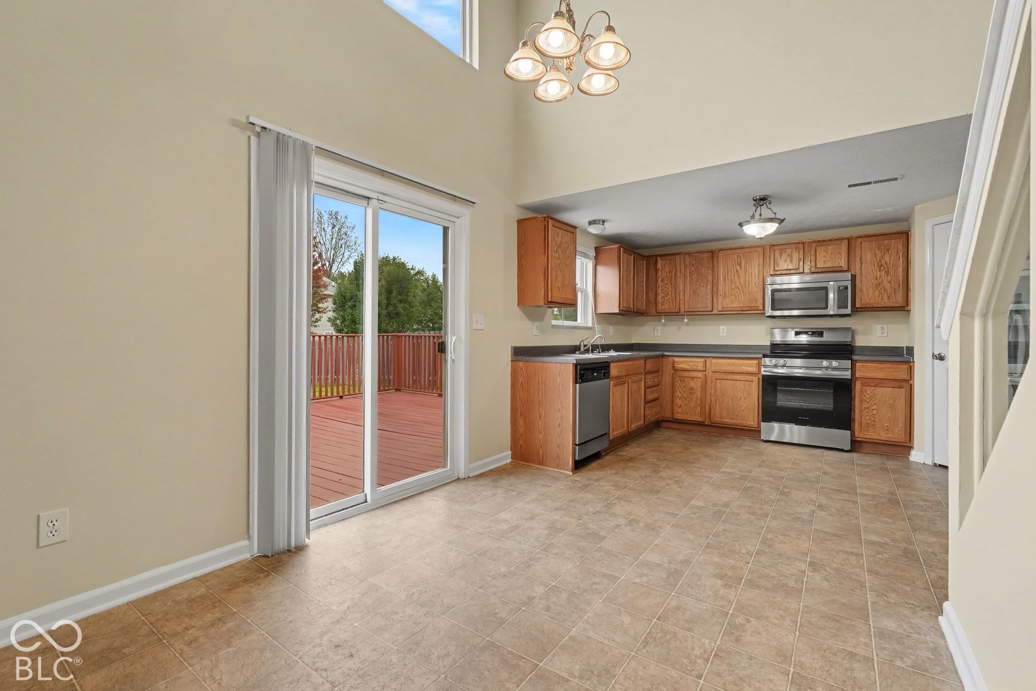 Kitchen featuring stained-wood cabinetry, stainless steel appliances, tile flooring, high ceilings, and sliding glass doors leading to an exterior deck
