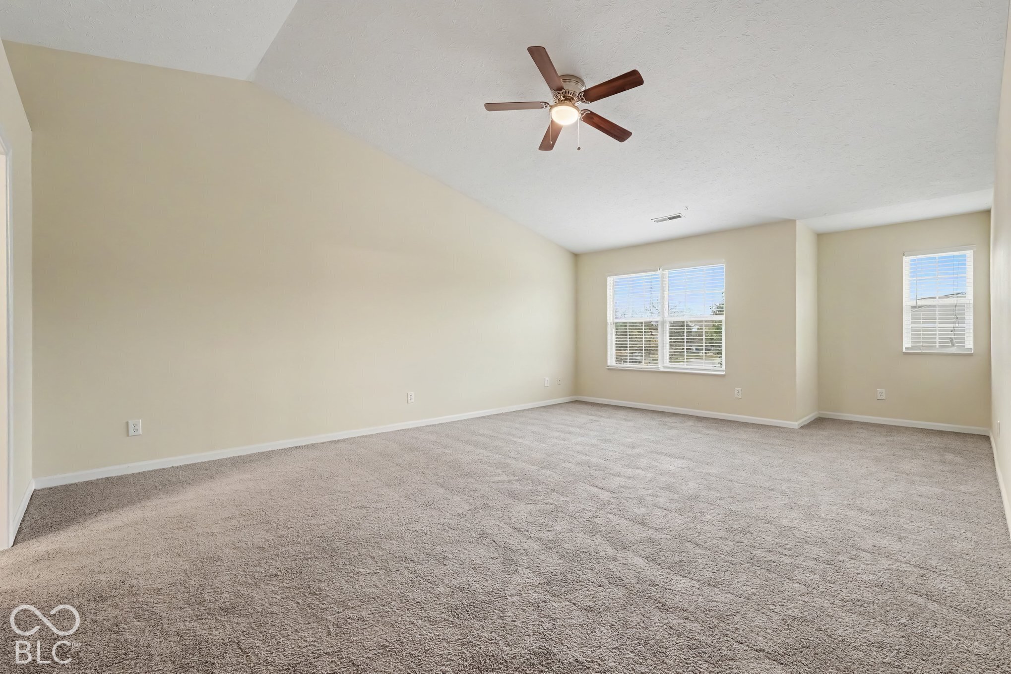 Vaulted ceiling, neutral wall tones, carpeted flooring, multi-pane windows, and a central ceiling fan with integrated lighting