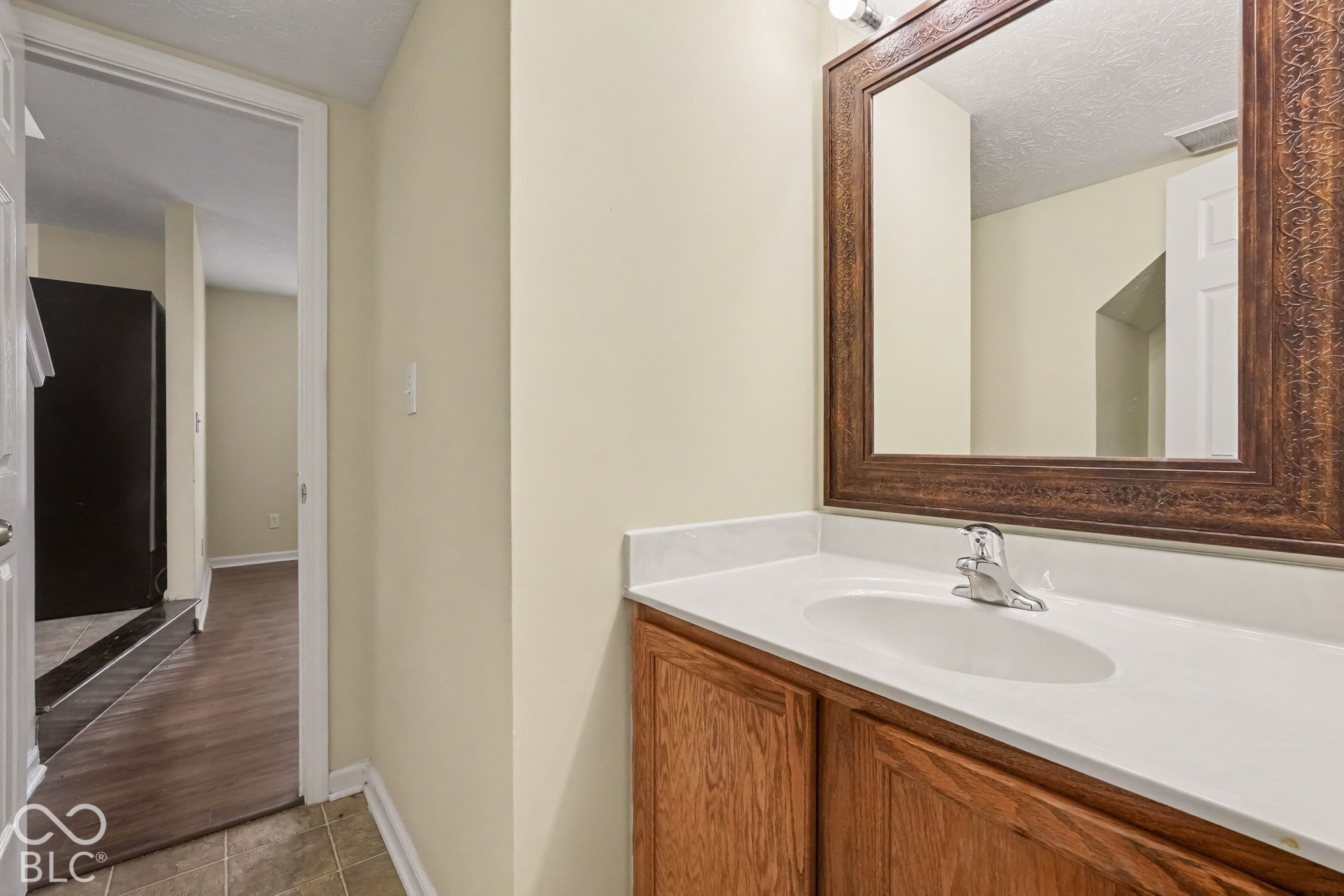 Vanity with wood-finish cabinetry, solid-surface countertop, integrated basin, chrome faucet, and decorative framed mirror