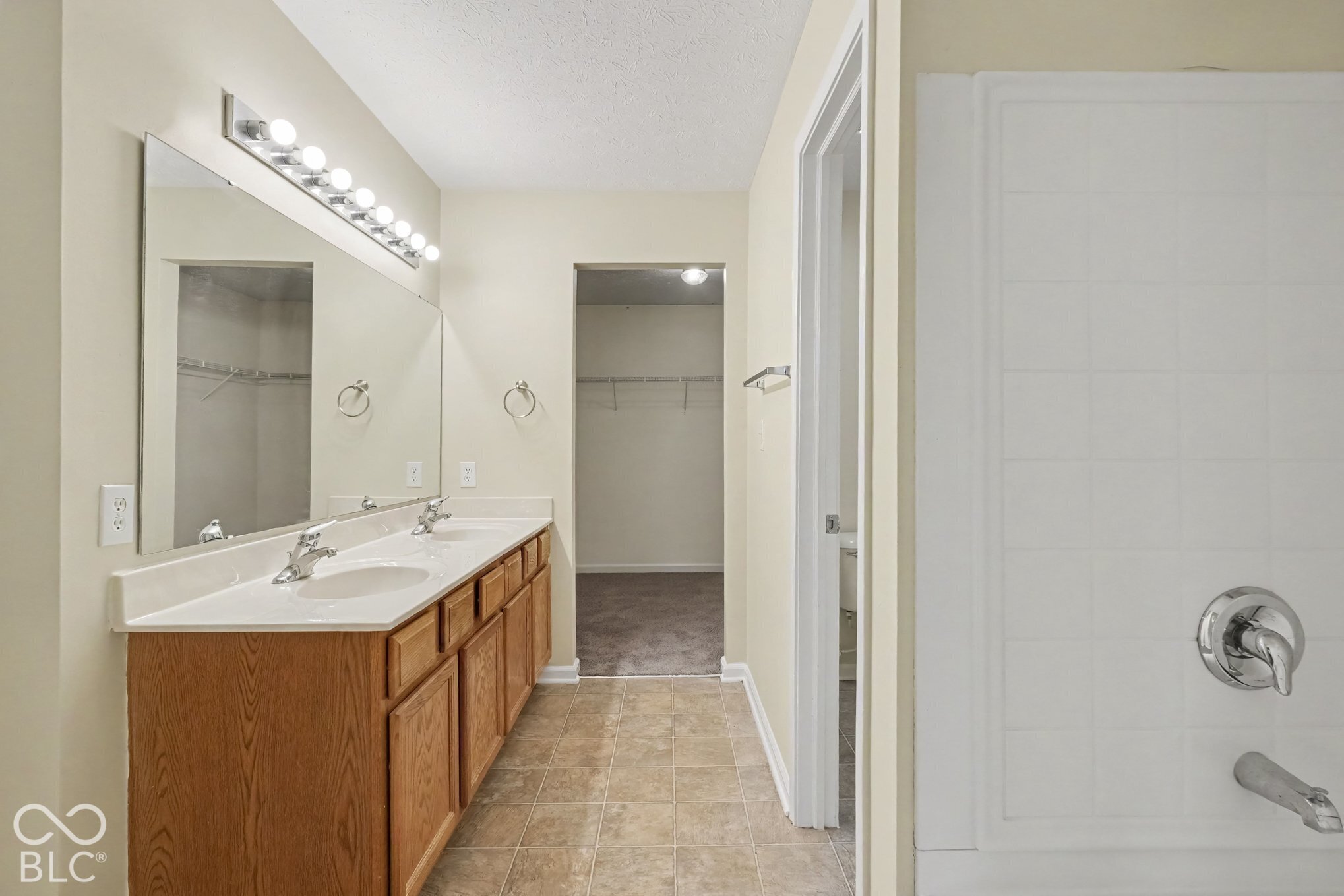 Bathroom featuring a double-sink vanity with wood-finish cabinetry, solid-surface countertop, full-width vanity mirror, tile-surround tub, and integrated storage area