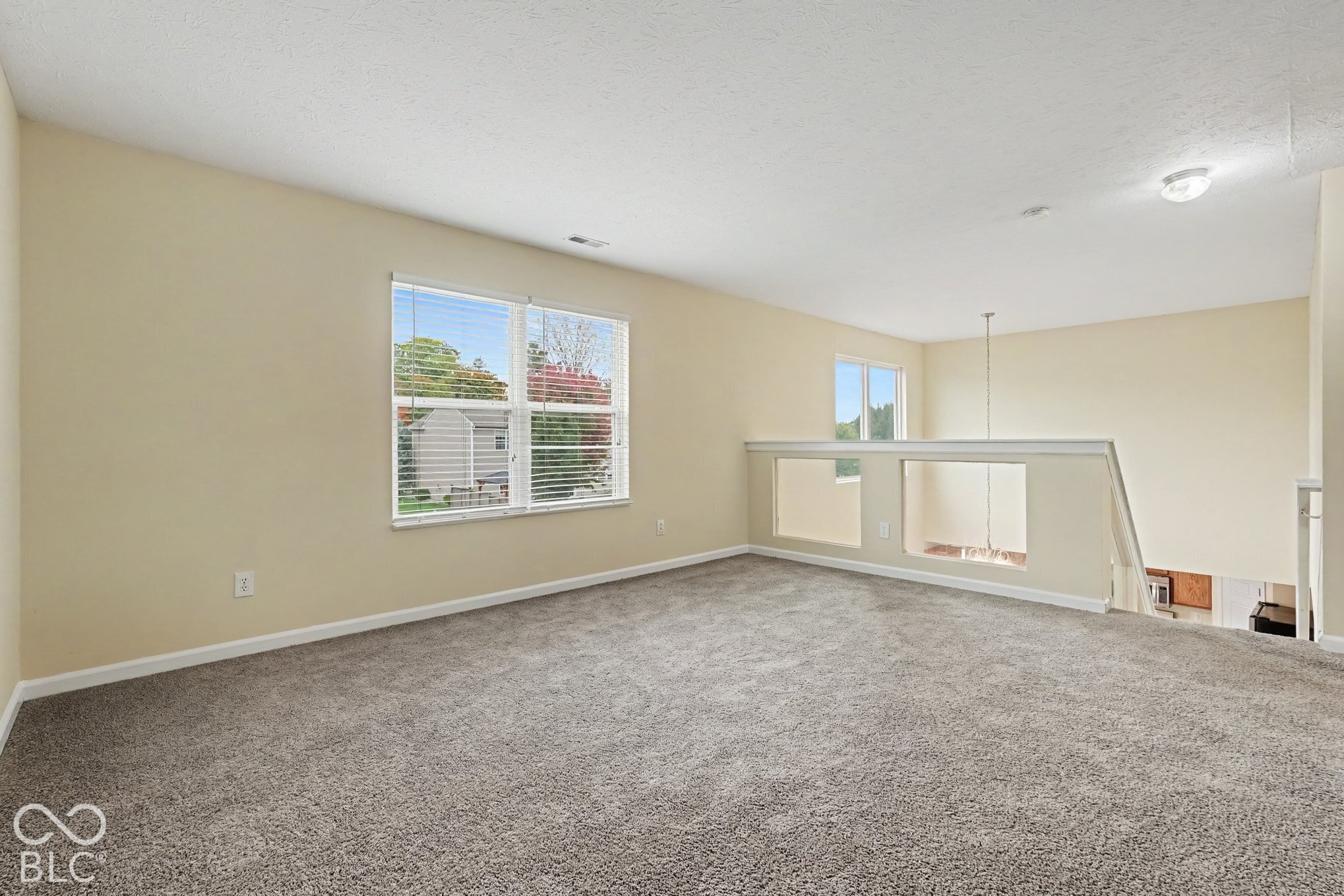 Open loft area featuring neutral wall-to-wall carpeting, multiple windows, and a partial pony wall with decorative trim