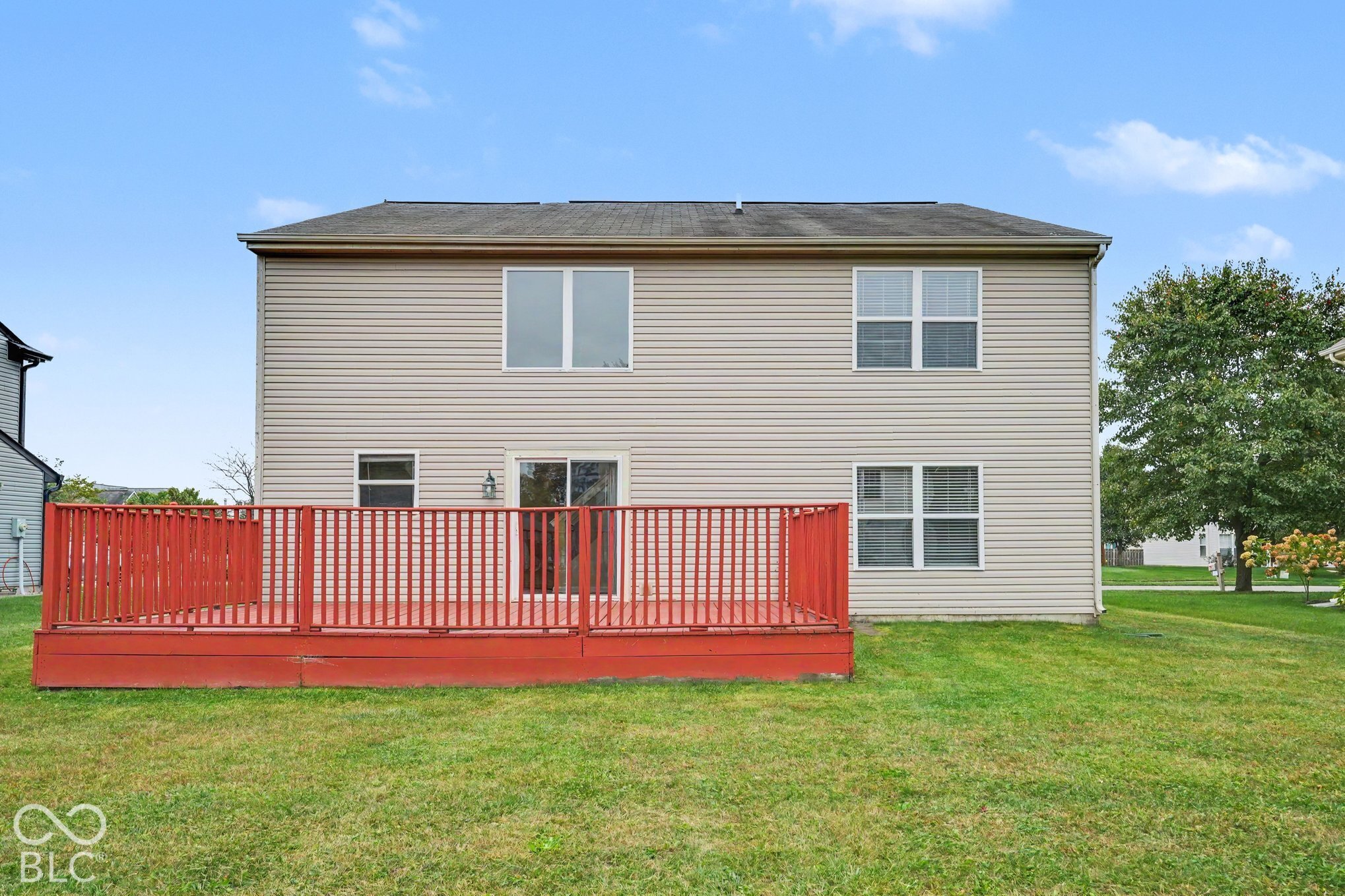 Two-story exterior with vinyl siding, shingled roof, sliding glass door, and a spacious raised wooden deck with railings
