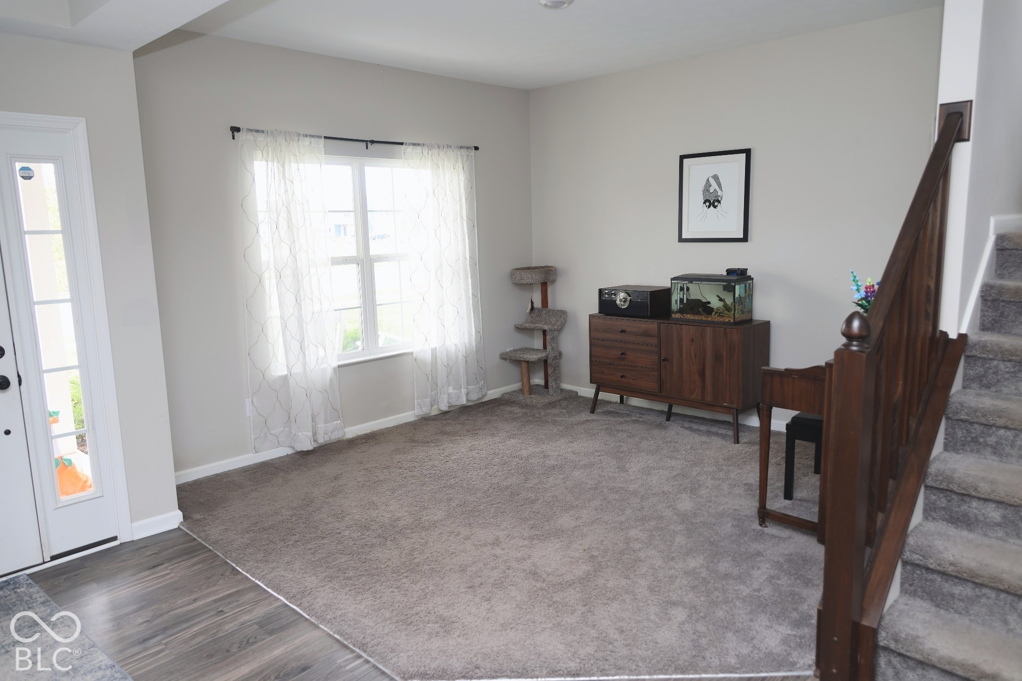 Interior space featuring wall-to-wall carpeting, wood-finish flooring at the entry, a multi-pane glass door, and a wooden handrail with a decorative newel post