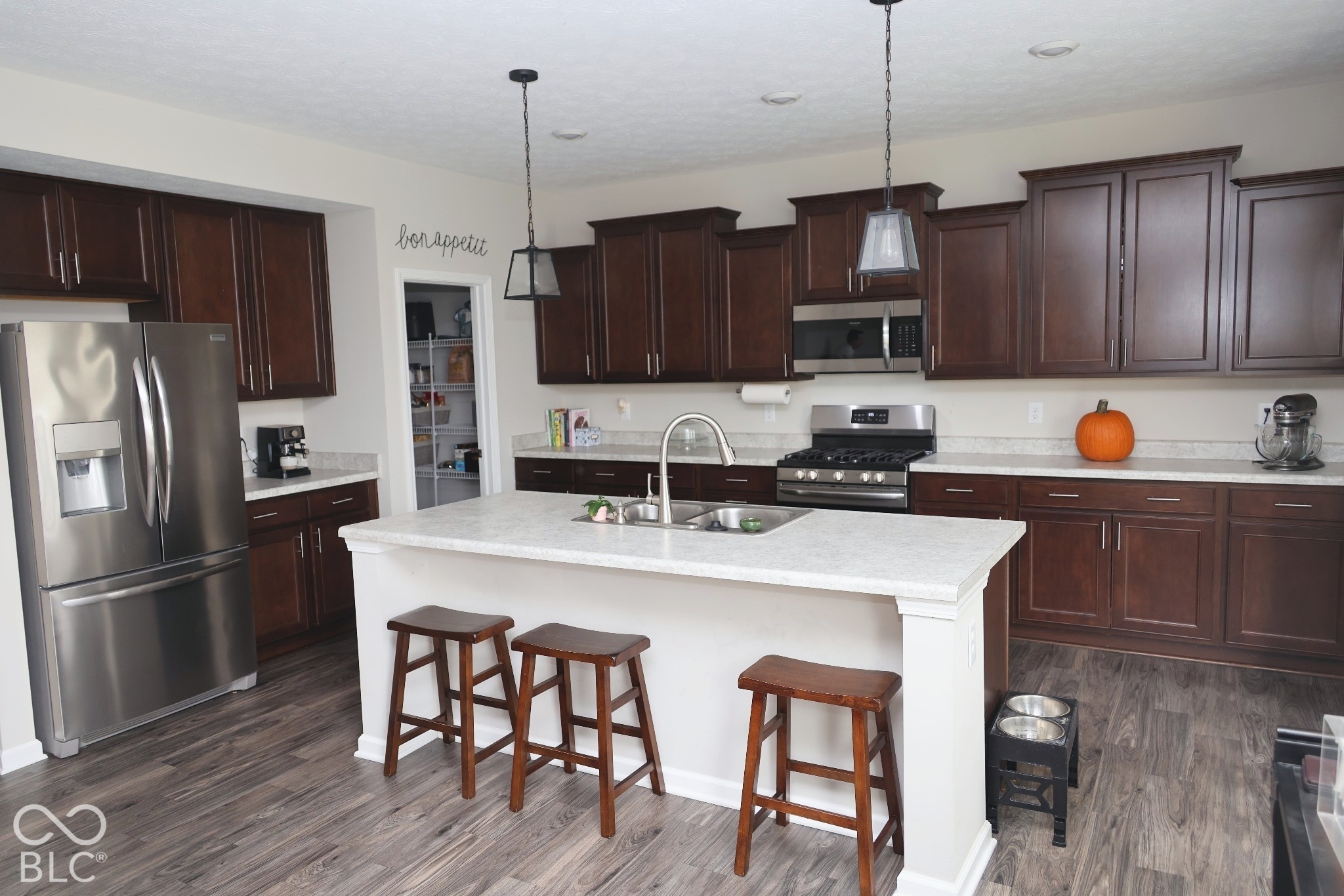 Kitchen featuring dark wood cabinetry, a central island with a stone-composite countertop, wood-finish flooring, stainless steel appliances, and dual pendant lighting
