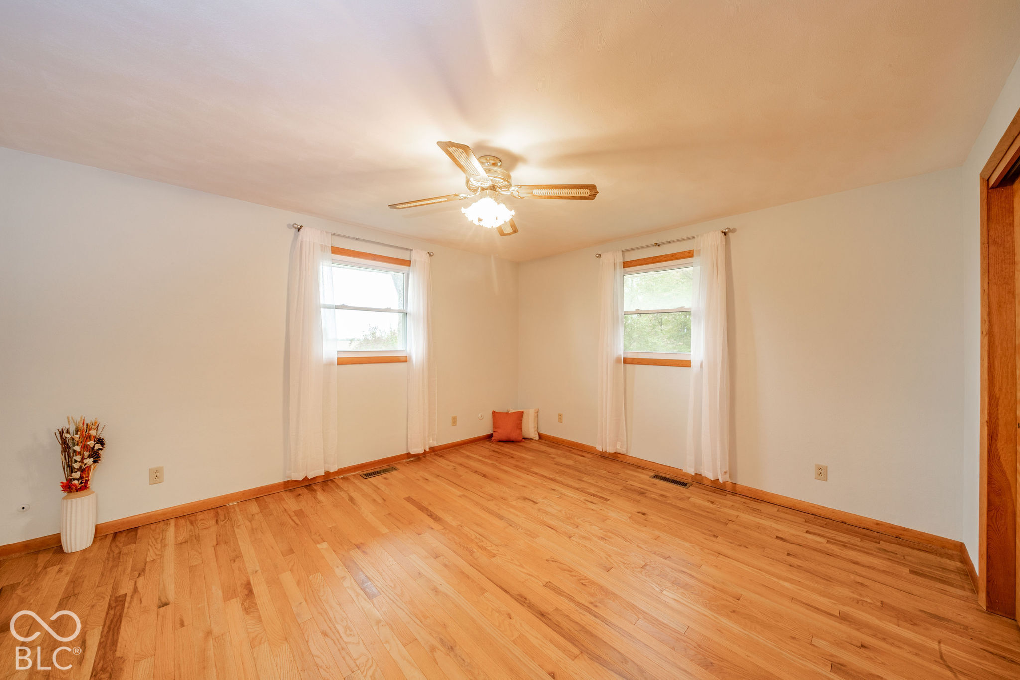 Interior space featuring wood-finish flooring, two windows with wood casing, and a ceiling-mounted light fixture with a fan