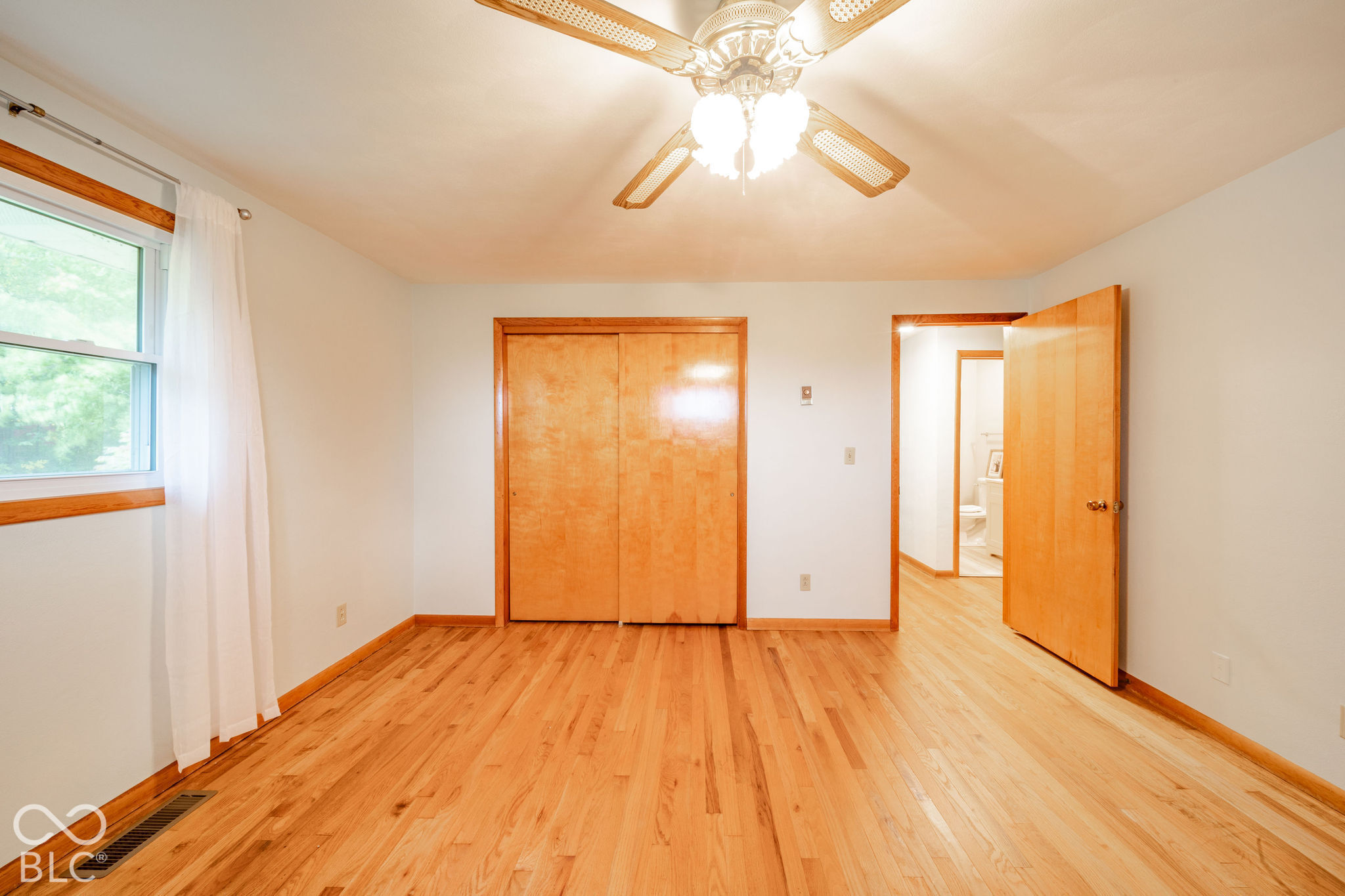 Wood-finish flooring, light wood-toned doors, dual-sliding closet doors, and a ceiling-mounted light fixture with a central fan