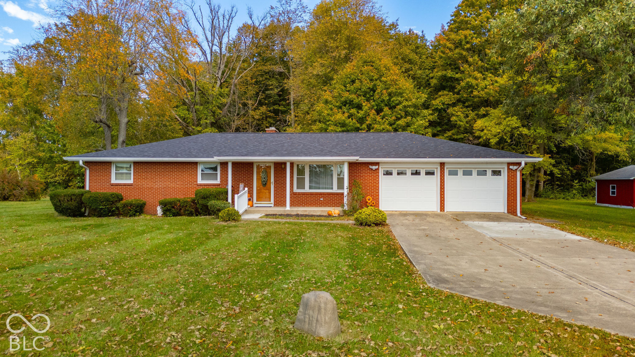Single-story brick exterior featuring a shingled roof, attached two-car garage, concrete driveway, and mature landscaping