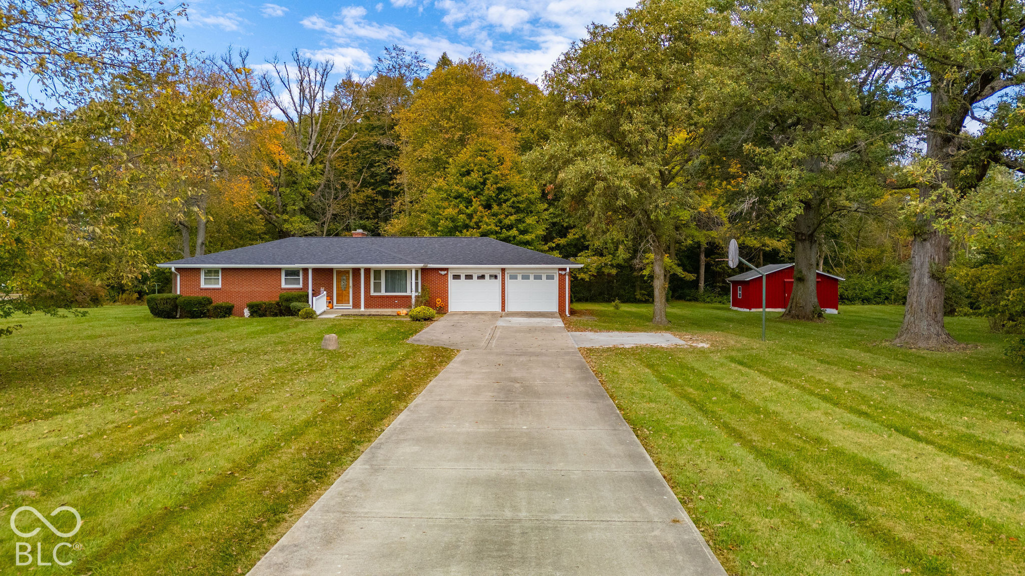 Single-story brick exterior featuring a multi-car garage, concrete driveway, and detached storage building situated on an expansive lot with mature trees Single-story brick exterior featuring a multi-car garage, concrete driveway, and detached storage building situated on an expansive lot with mature trees