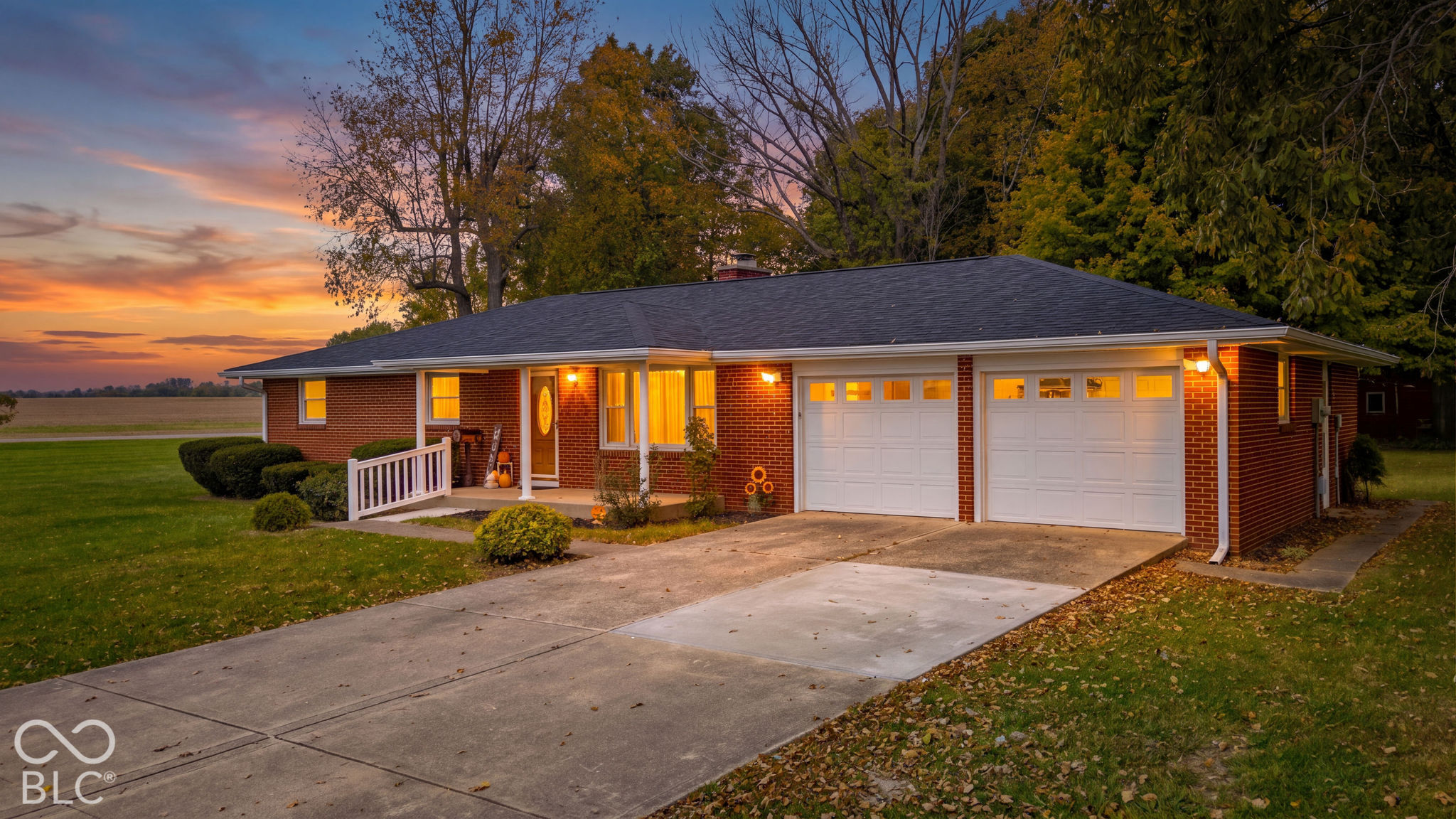 Red brick exterior featuring a covered front porch, attached two-car garage with white paneled doors, and concrete driveway