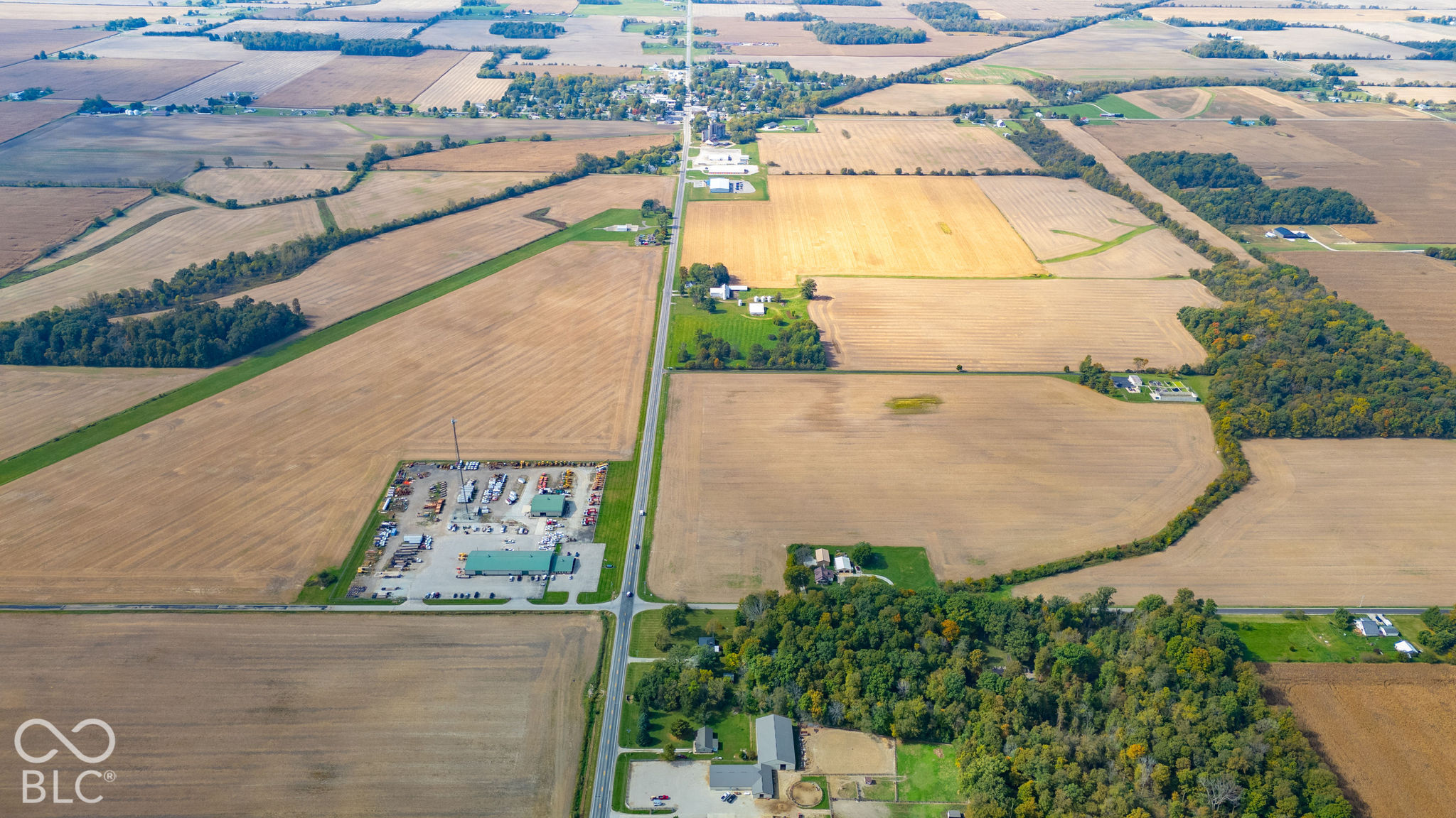Aerial perspective showcasing expansive acreage, vast open fields, mature wooded borders, and direct road access