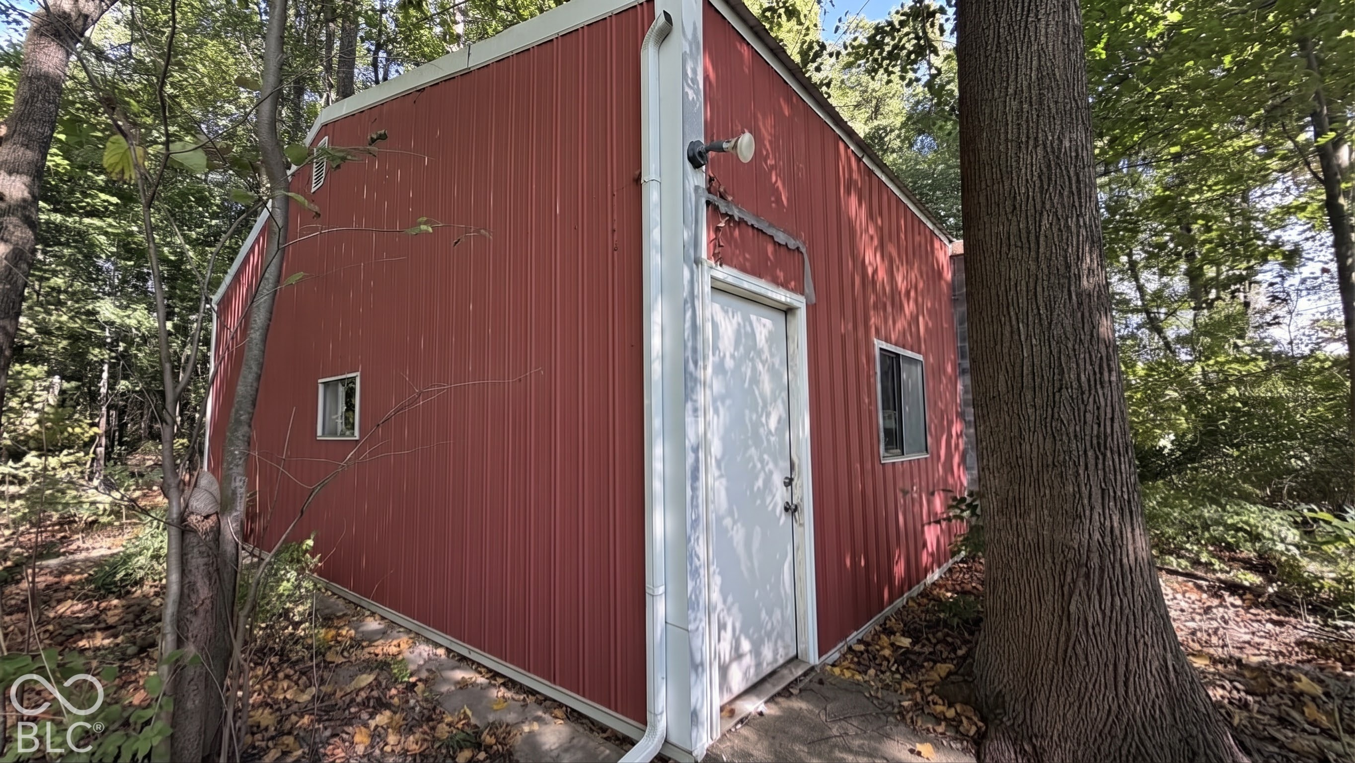 Detached outbuilding featuring vertical metal siding, a solid entry door, framed windows, and exterior mounted lighting