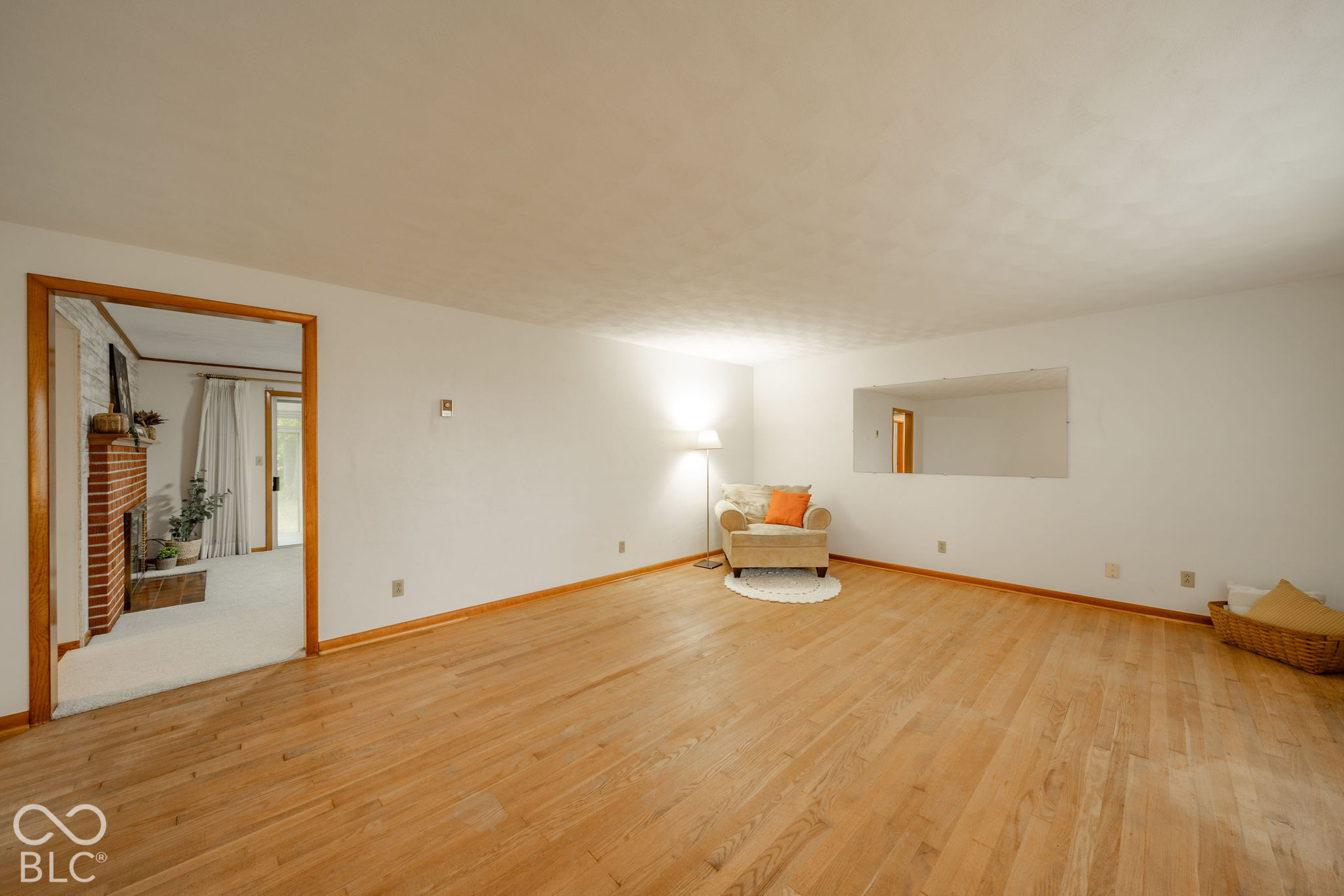 Interior space featuring wood-finish flooring, a wall-mounted rectangular mirror, and an exposed brick masonry fireplace Interior space featuring wood-finish flooring, a wall-mounted rectangular mirror, and an exposed brick masonry fireplace