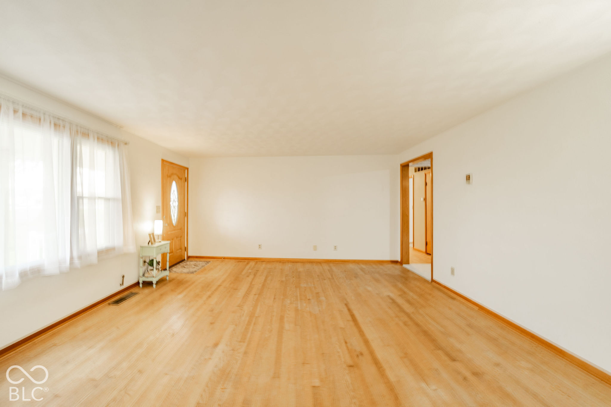 Spacious room featuring wood-finish flooring, neutral wall paint, and a solid wood front door with an oval glass insert Spacious room featuring wood-finish flooring, neutral wall paint, and a solid wood front door with an oval glass insert