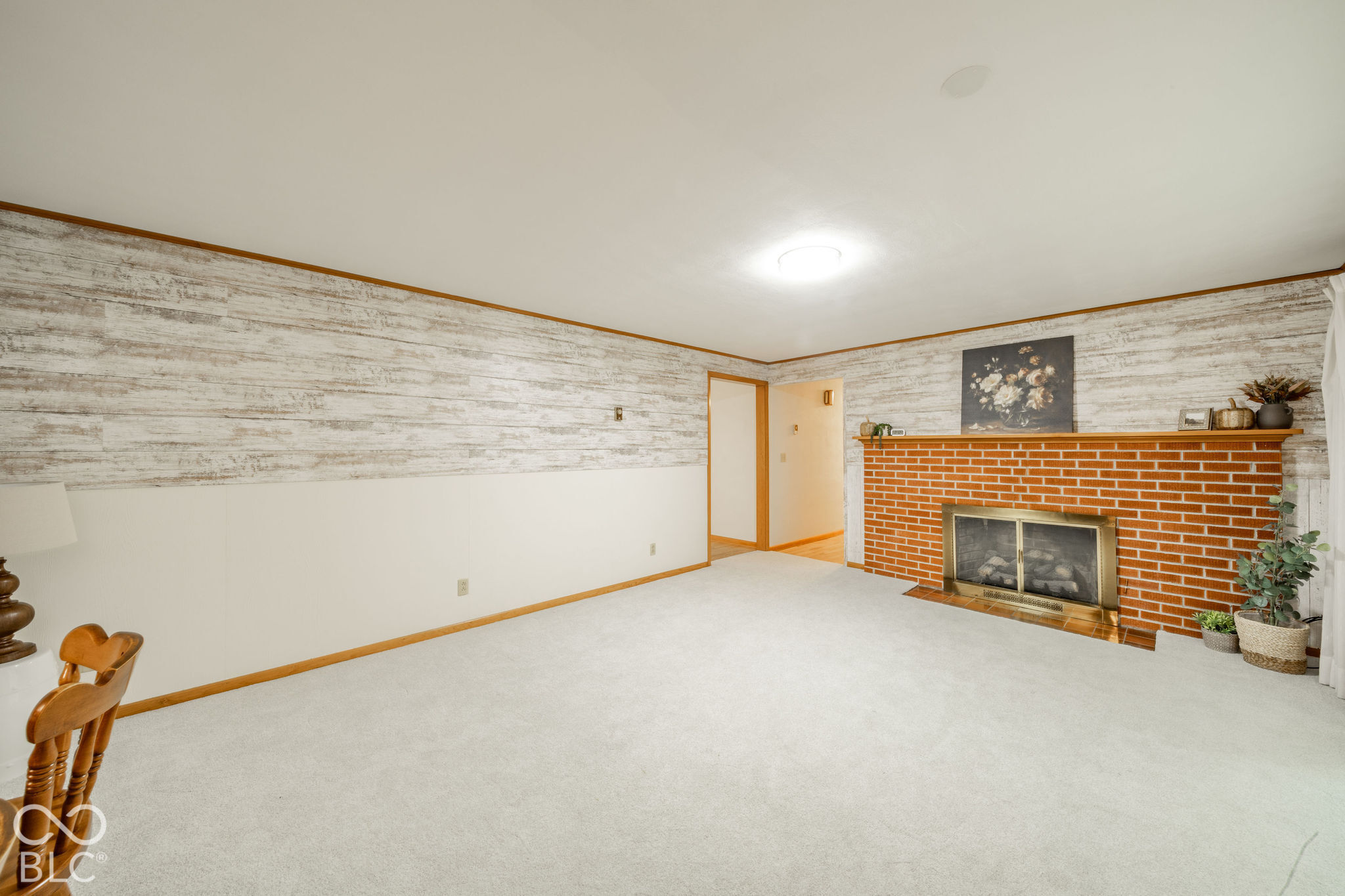 Living area featuring a floor-to-ceiling brick fireplace with a wood mantel, rustic-finish horizontal plank wall paneling, and wall-to-wall carpeting