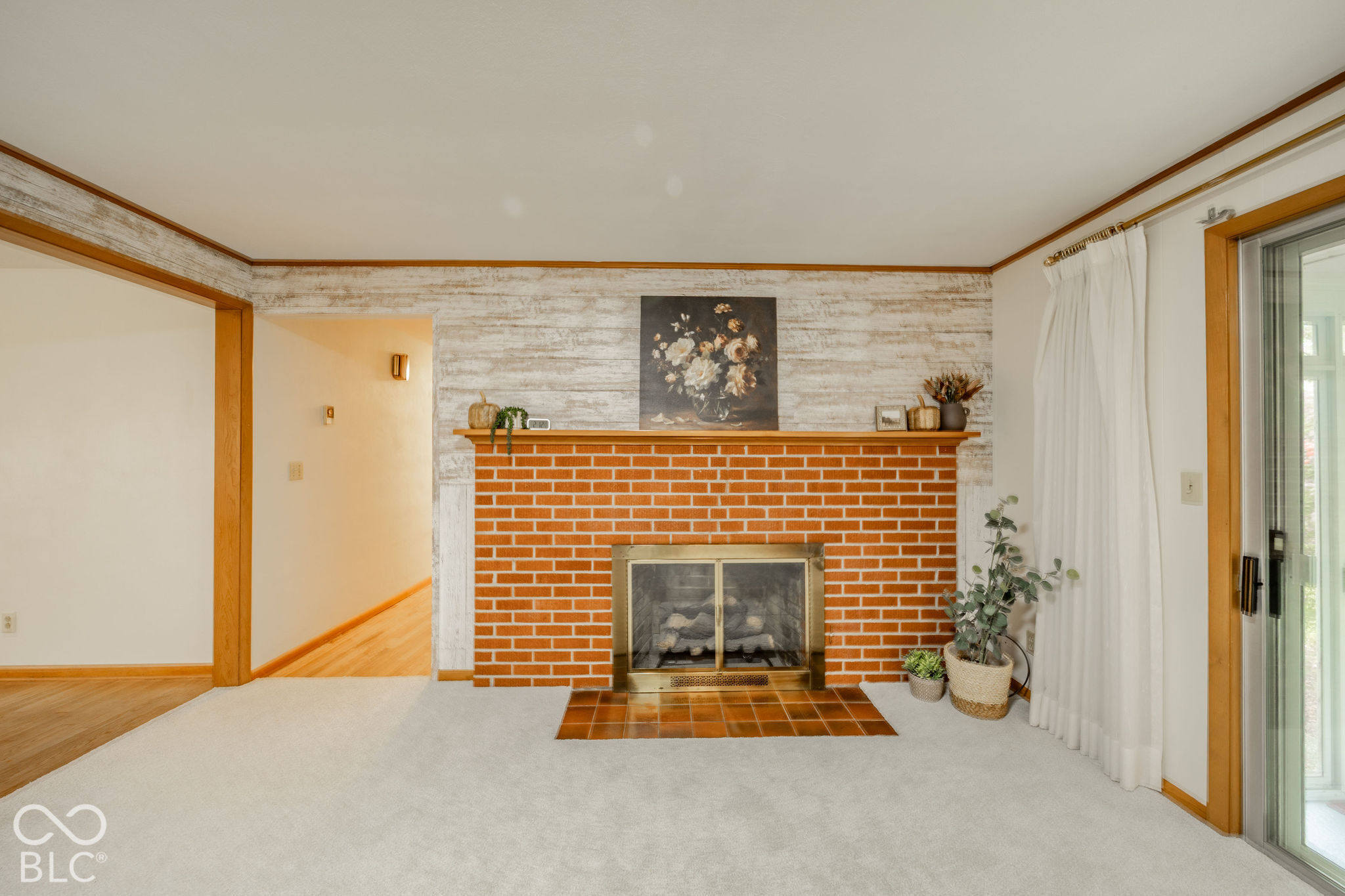 Fireplace featuring a red brick surround, wood mantel, metal hearth screen, and tile floor pad, accompanied by a textured accent wall Fireplace featuring a red brick surround, wood mantel, metal hearth screen, and tile floor pad, accompanied by a textured accent wall