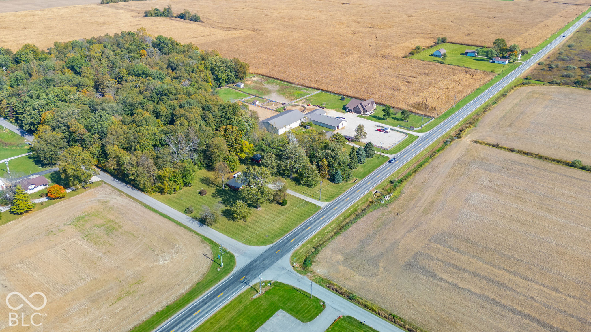 Aerial perspective featuring a large tract of land with mature trees, expansive open fields, and paved road frontage