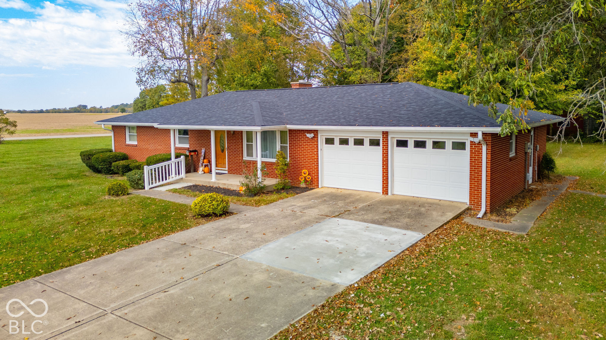 Brick exterior residence featuring a covered front porch, attached two-car garage with paneled doors, and concrete driveway on a large lot