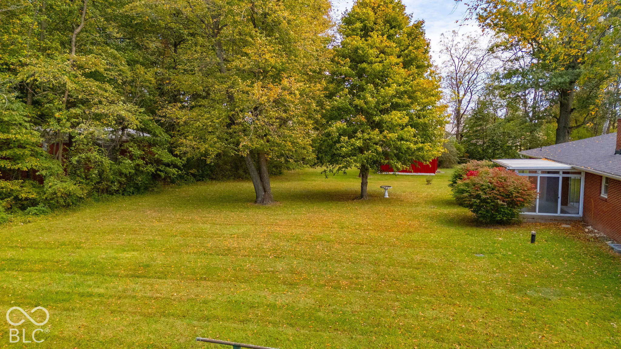 Expansive backyard featuring mature trees, a red exterior outbuilding, and an attached glass-enclosed patio with a red brick facade