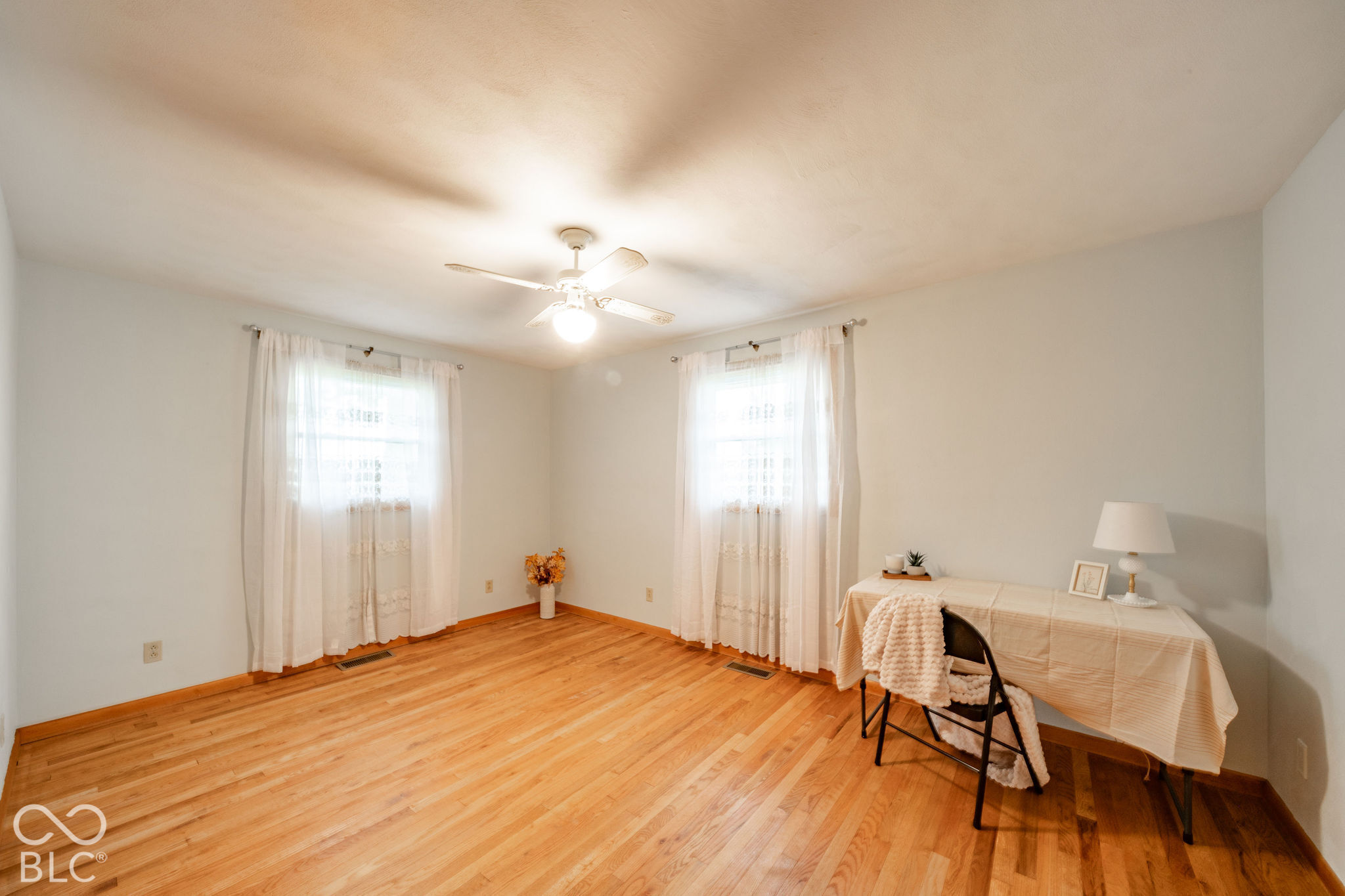 Room featuring natural wood-finish flooring, two dual-pane windows with hardware, and a white ceiling-mounted fan with integrated light fixture