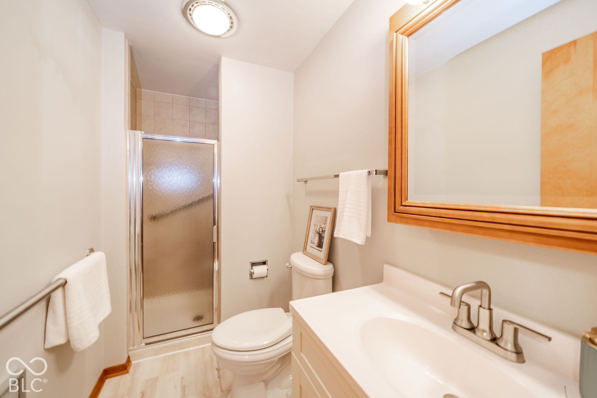 Bathroom featuring a shower stall with a textured glass door, a vanity with a white integrated sink, a brushed nickel faucet, wood-finished cabinetry, and a wood-framed wall mirror