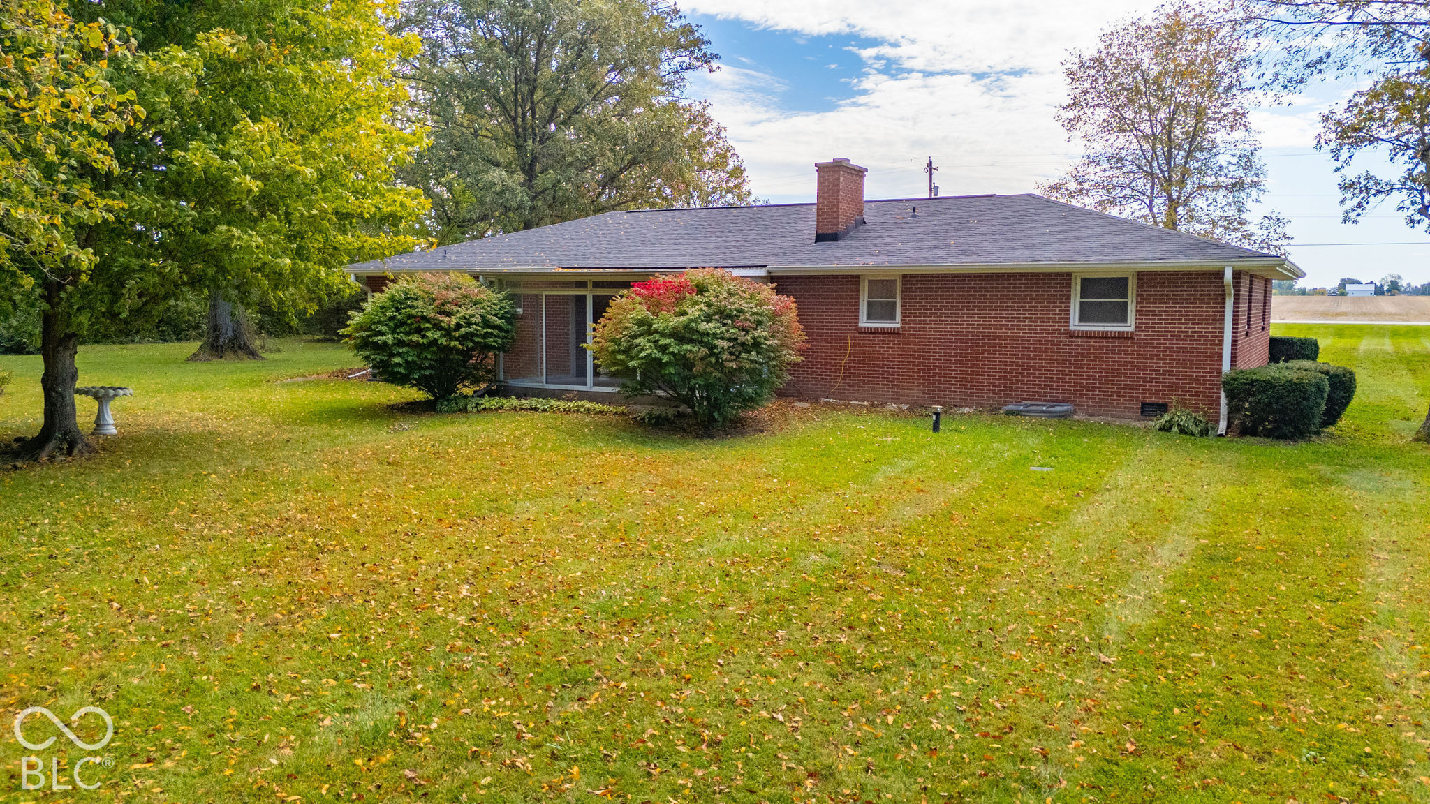 Single-story brick exterior featuring a shingled hip roof, a central brick chimney, a sliding glass door, and an expansive lawn with mature trees
