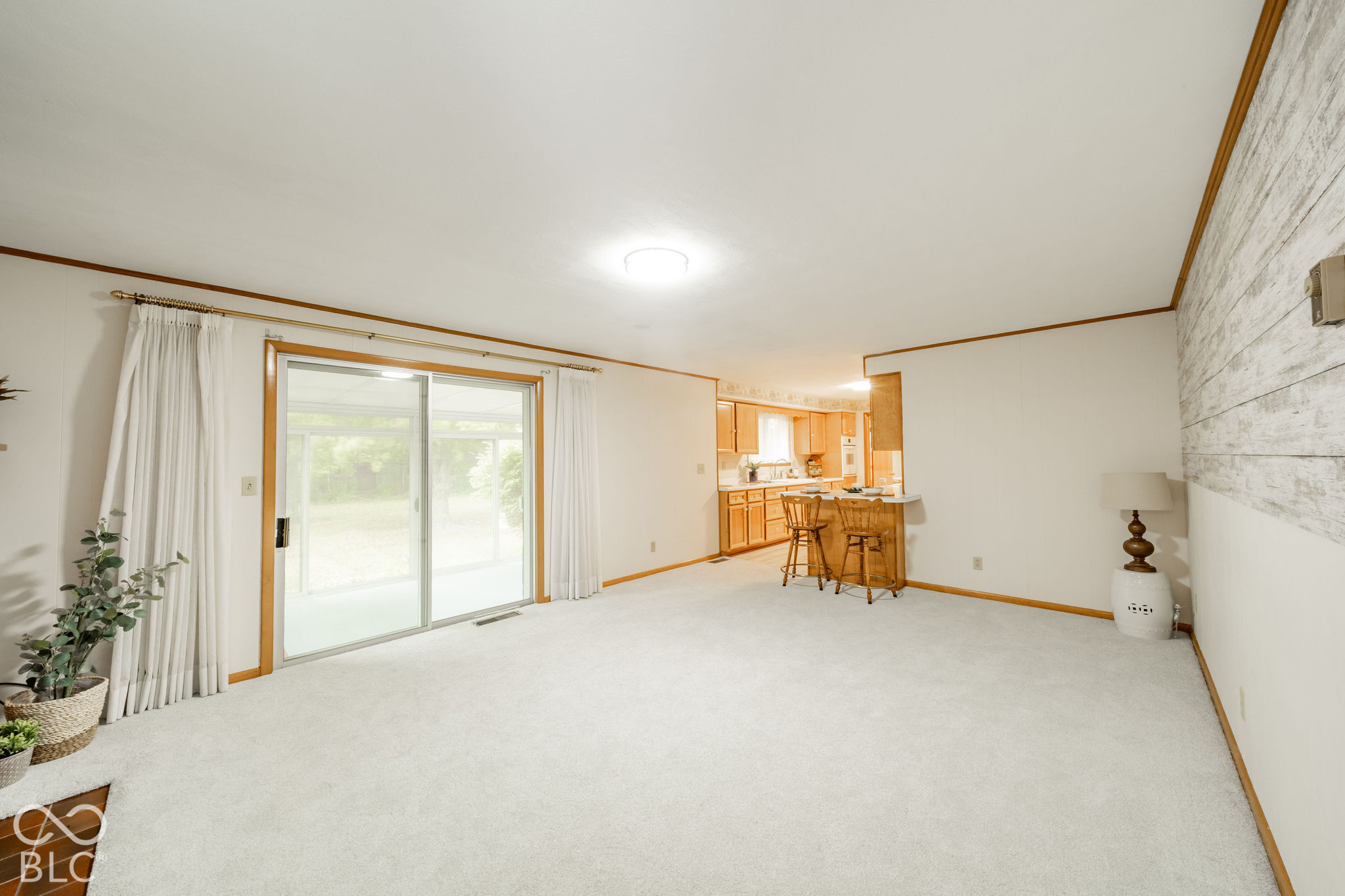 Open-concept living space featuring a sliding glass door, white wall-to-wall carpeting, and a decorative wood-plank accent wall Open-concept living space featuring a sliding glass door, white wall-to-wall carpeting, and a decorative wood-plank accent wall