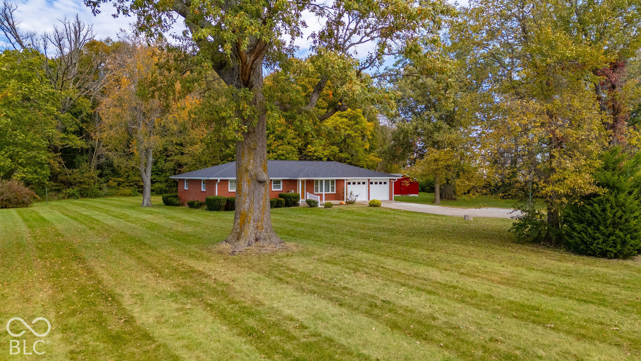 Single-story brick residence featuring a concrete driveway, two-car garage, and expansive lawn with mature trees