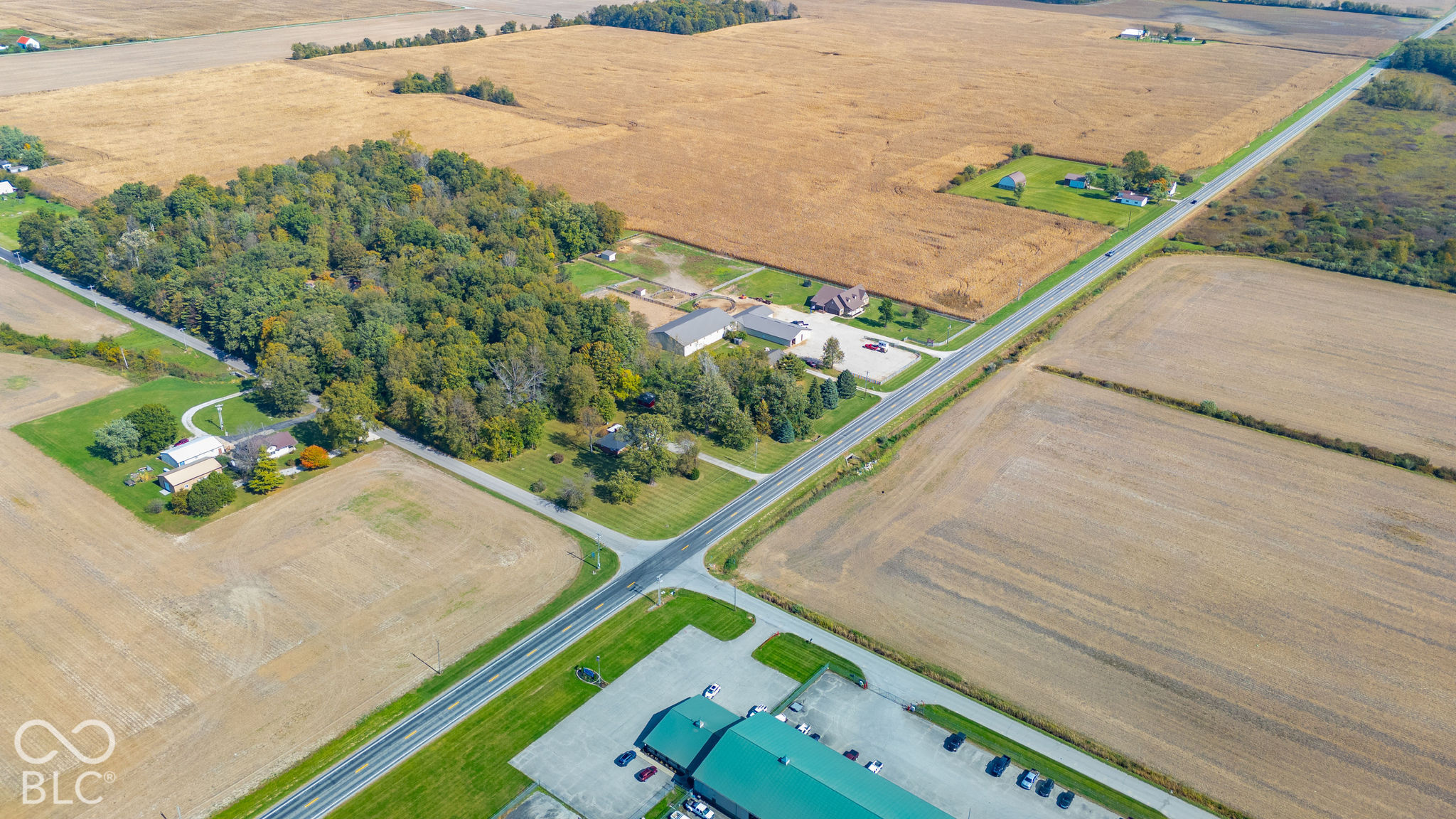 Aerial perspective of sprawling acreage featuring mature timber stands, expansive open fields, and paved road frontage