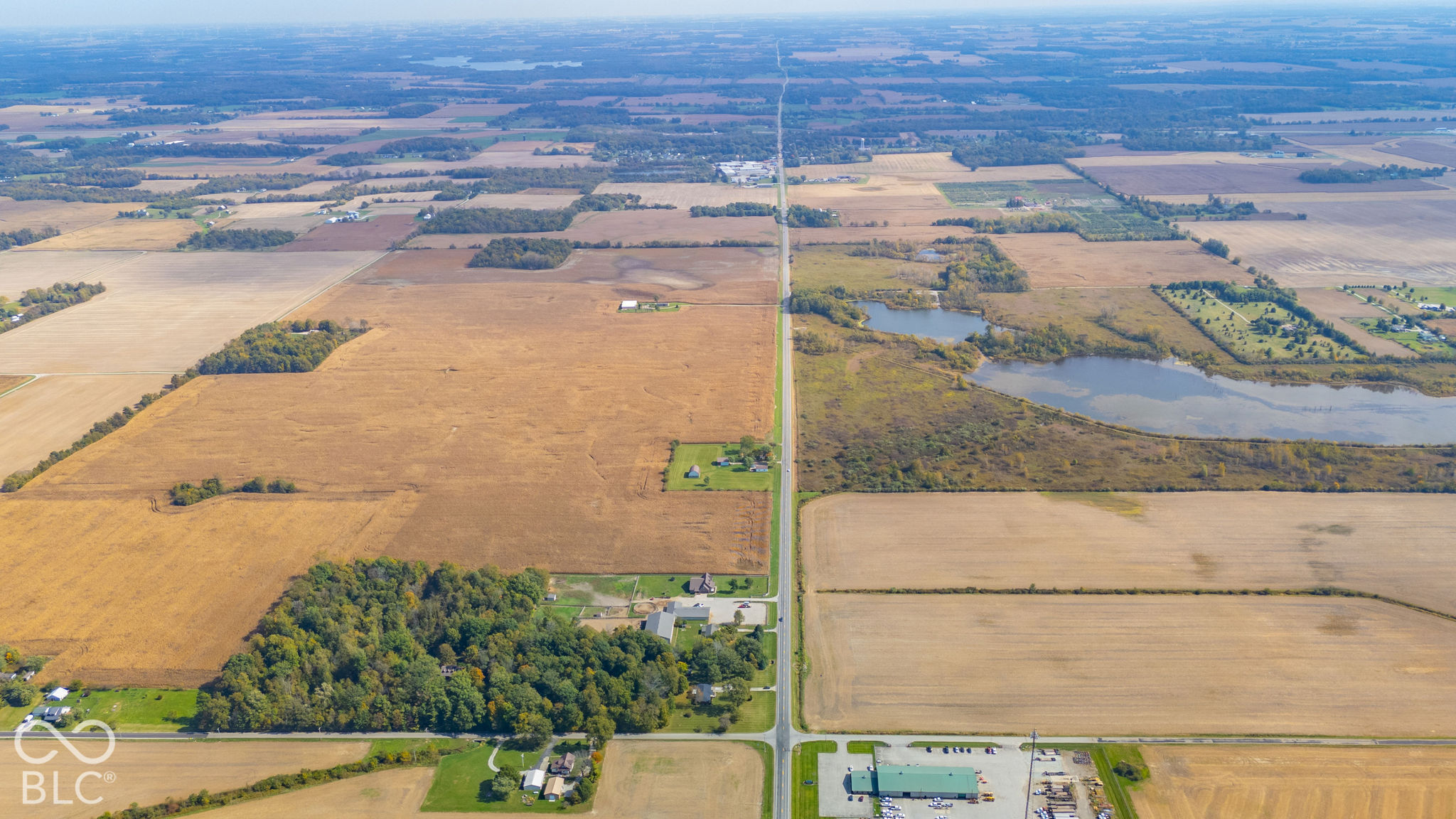 Aerial perspective of expansive acreage featuring vast agricultural land, mature tree clusters, and a private pond