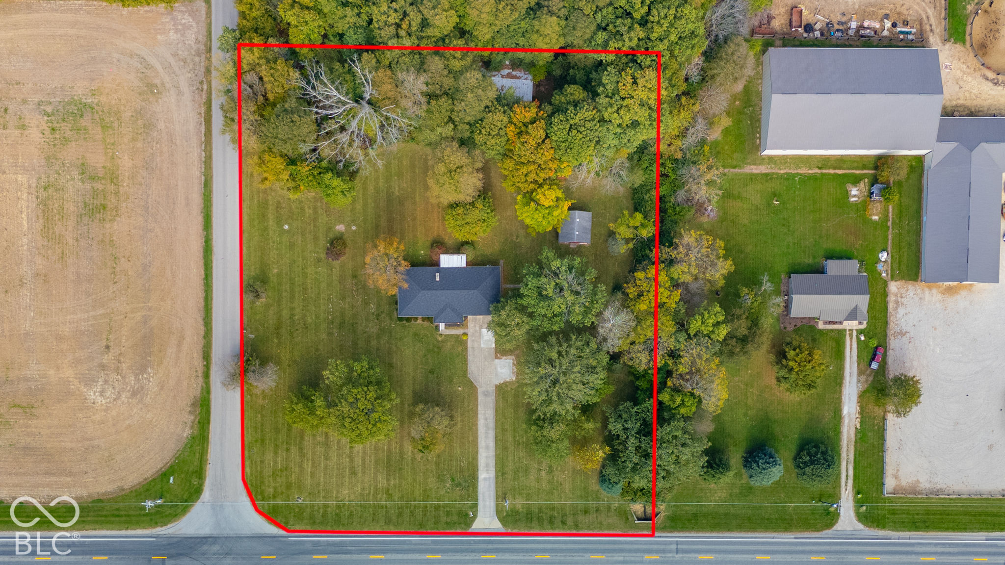 Aerial perspective featuring a spacious parcel of land, mature trees, a detached structure, and a paved driveway