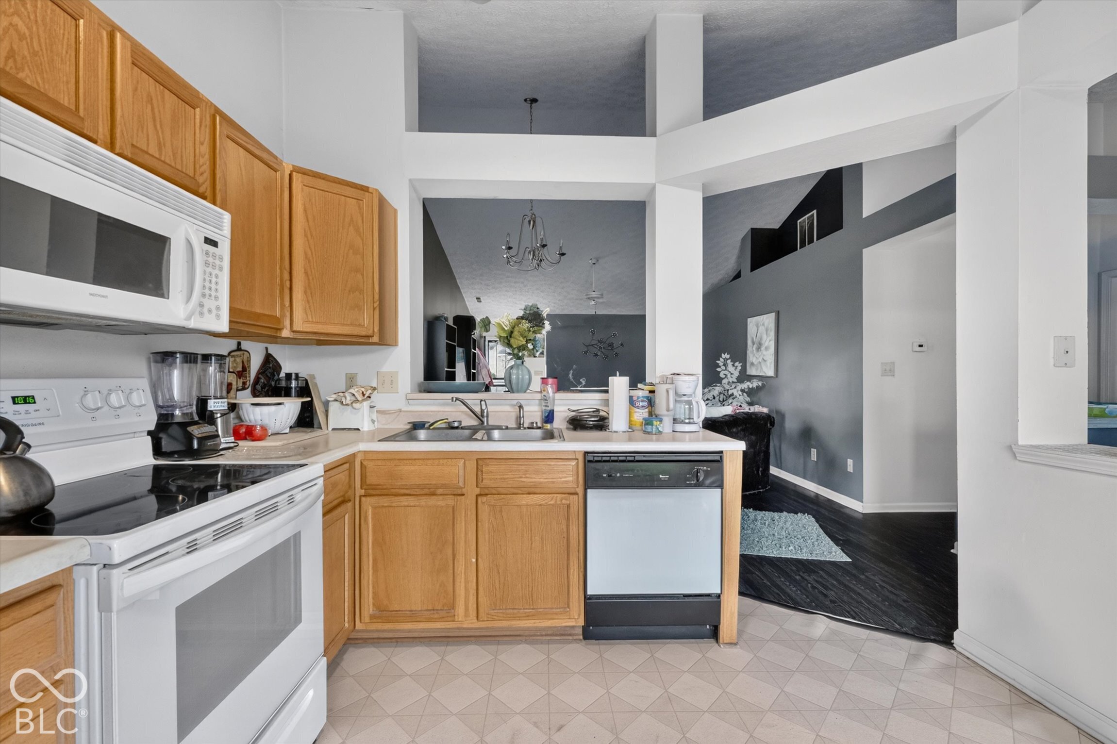 Kitchen featuring wood cabinetry, white appliances, dual-basin sink, and vaulted ceilings