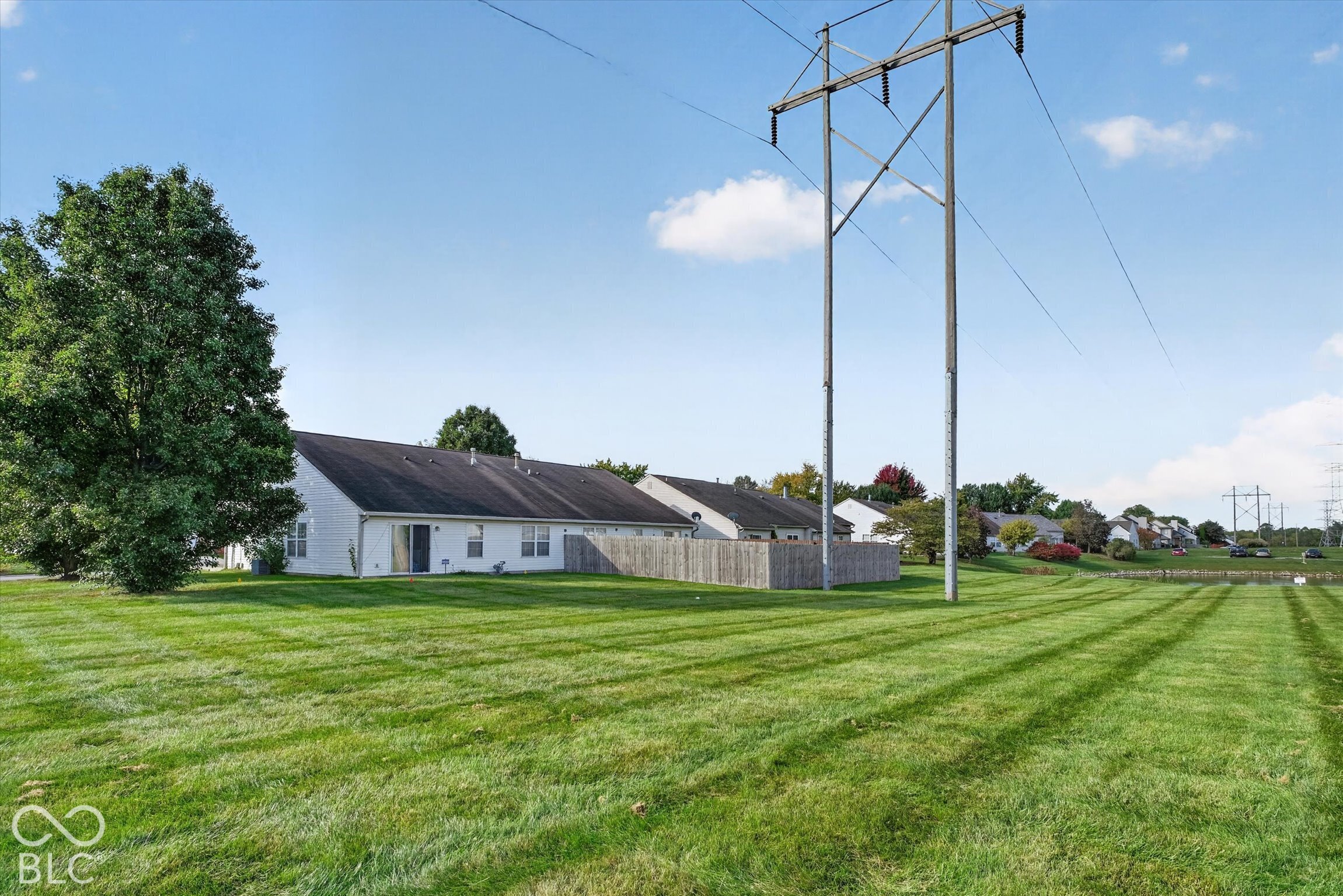 Expansive green space featuring mature trees and a partial wood fence enclosure