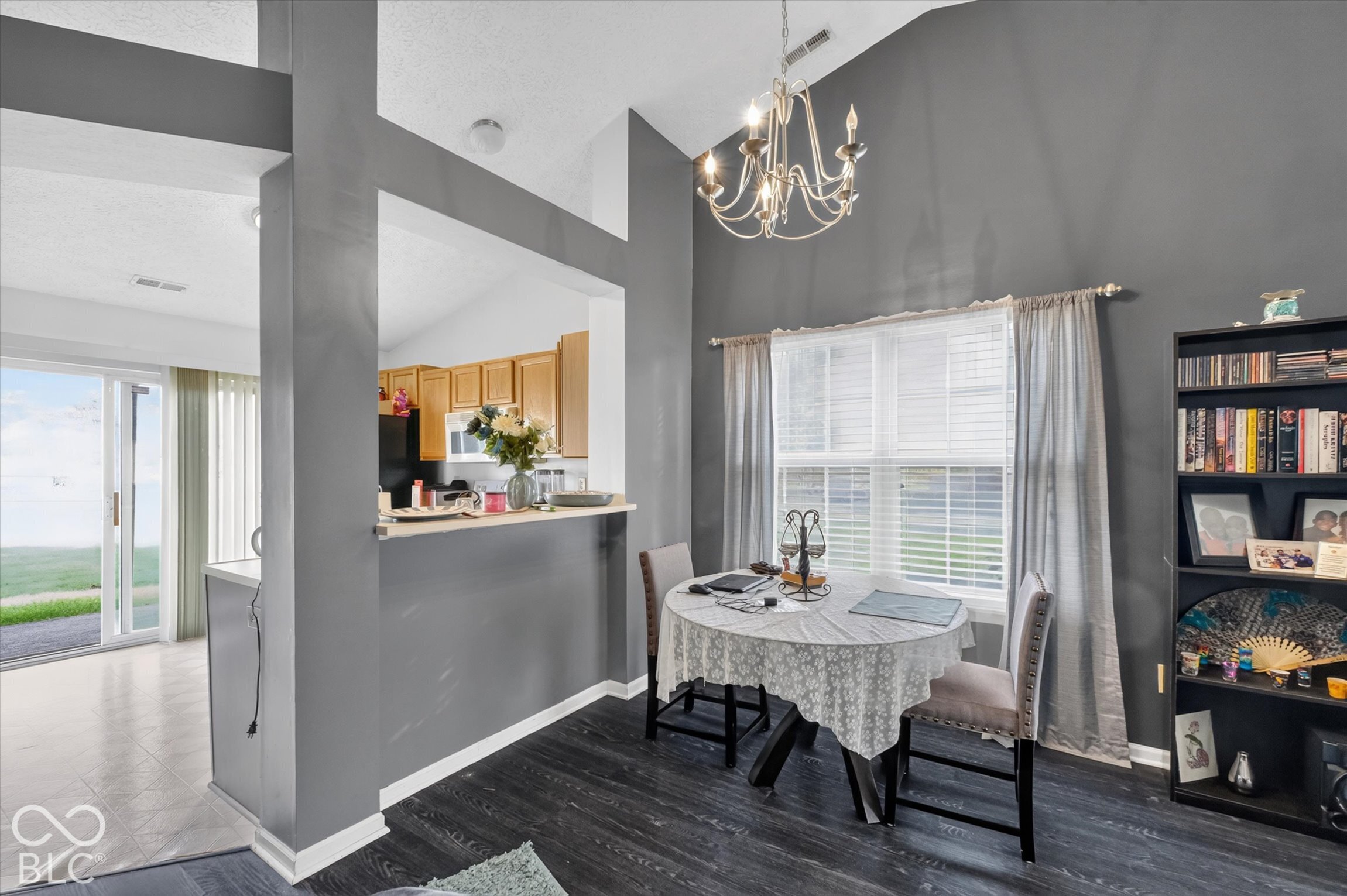 Vaulted ceiling featuring a multi-arm chandelier, wood-finish flooring, and a pass-through opening with a breakfast bar