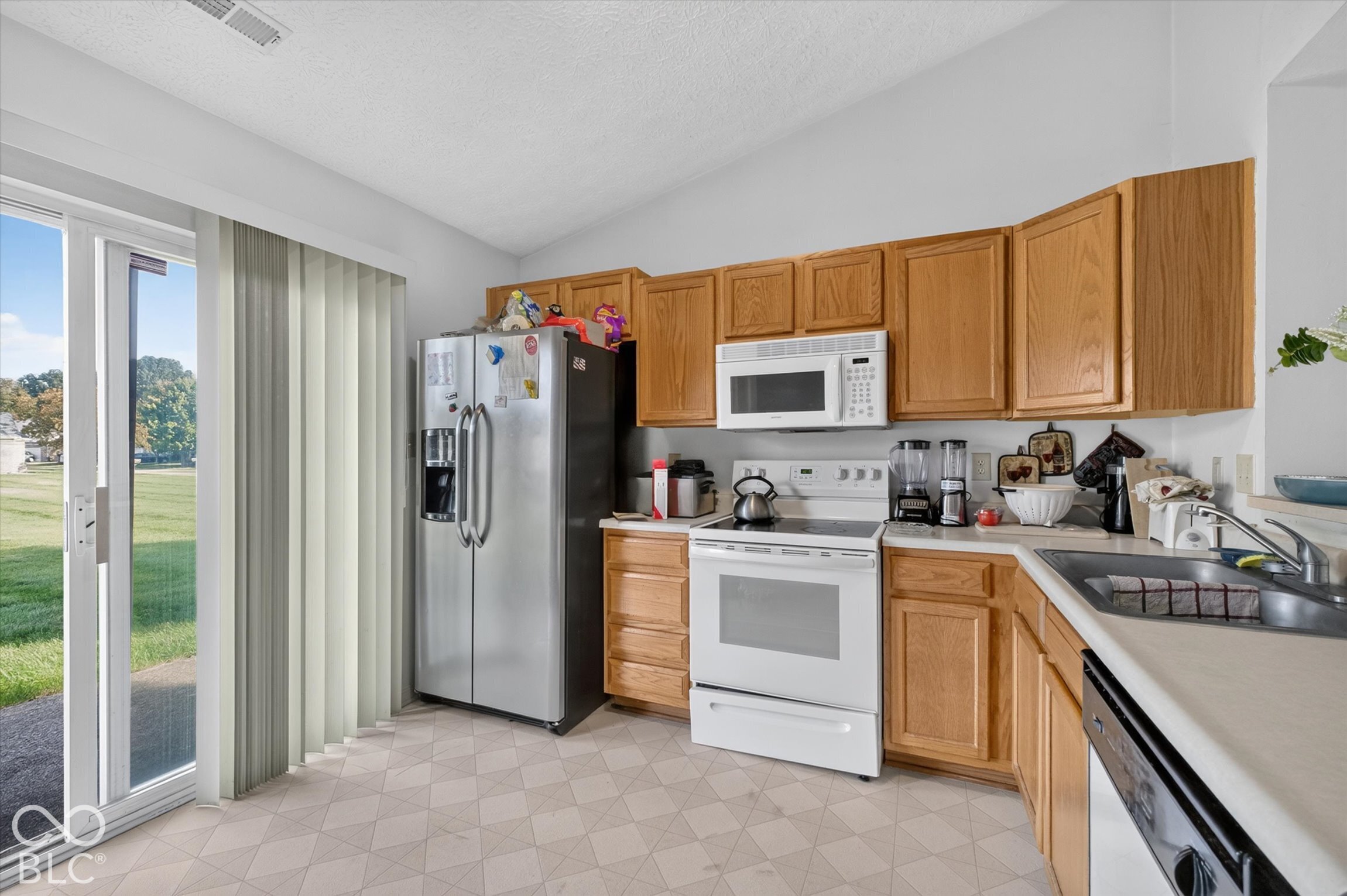 Kitchen featuring natural finish wood cabinetry, stainless steel refrigerator, white appliance suite, and sliding glass doors