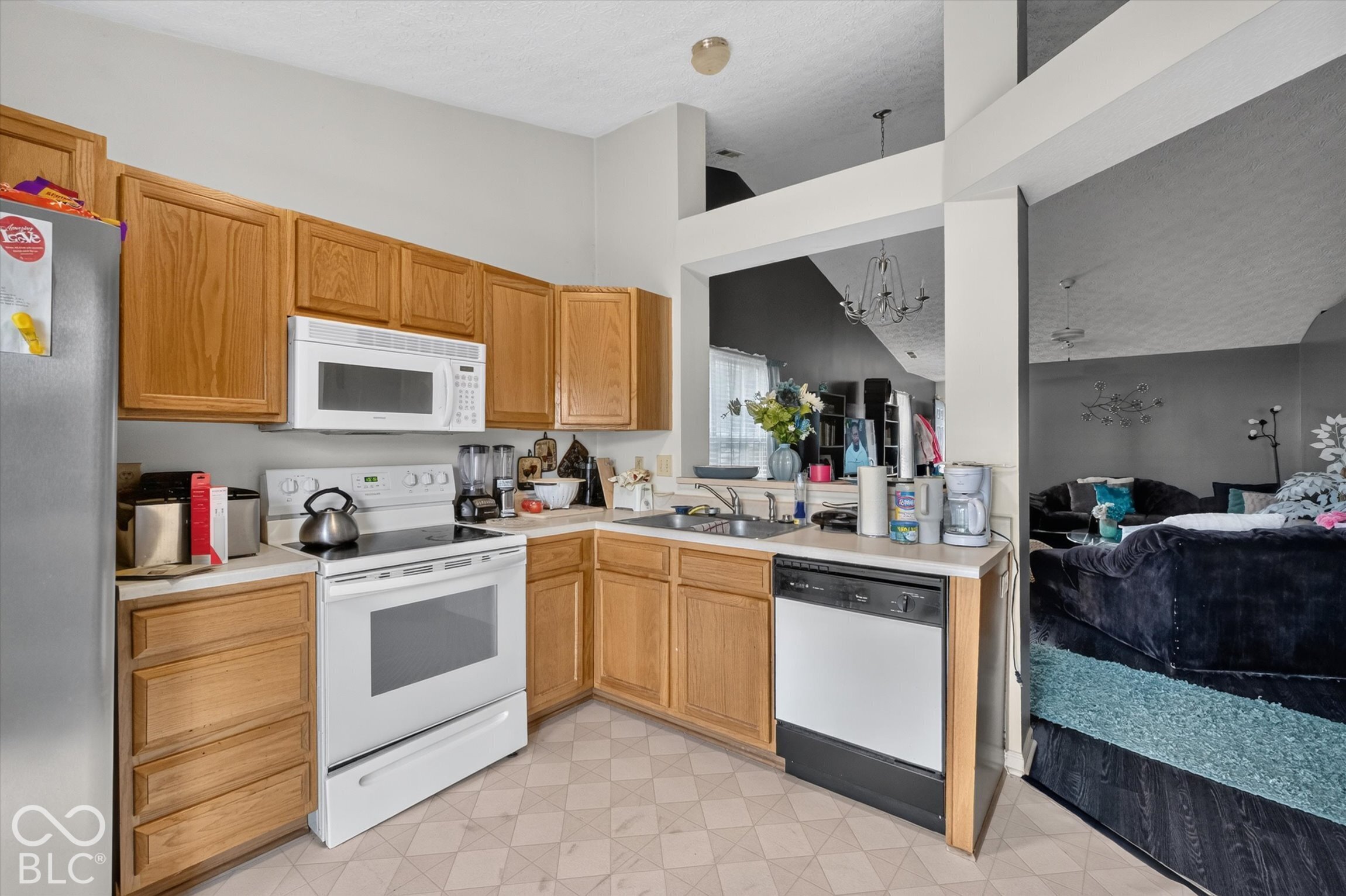 Kitchen featuring wood cabinetry, white appliances, a double-basin stainless steel sink, and geometric-patterned flooring