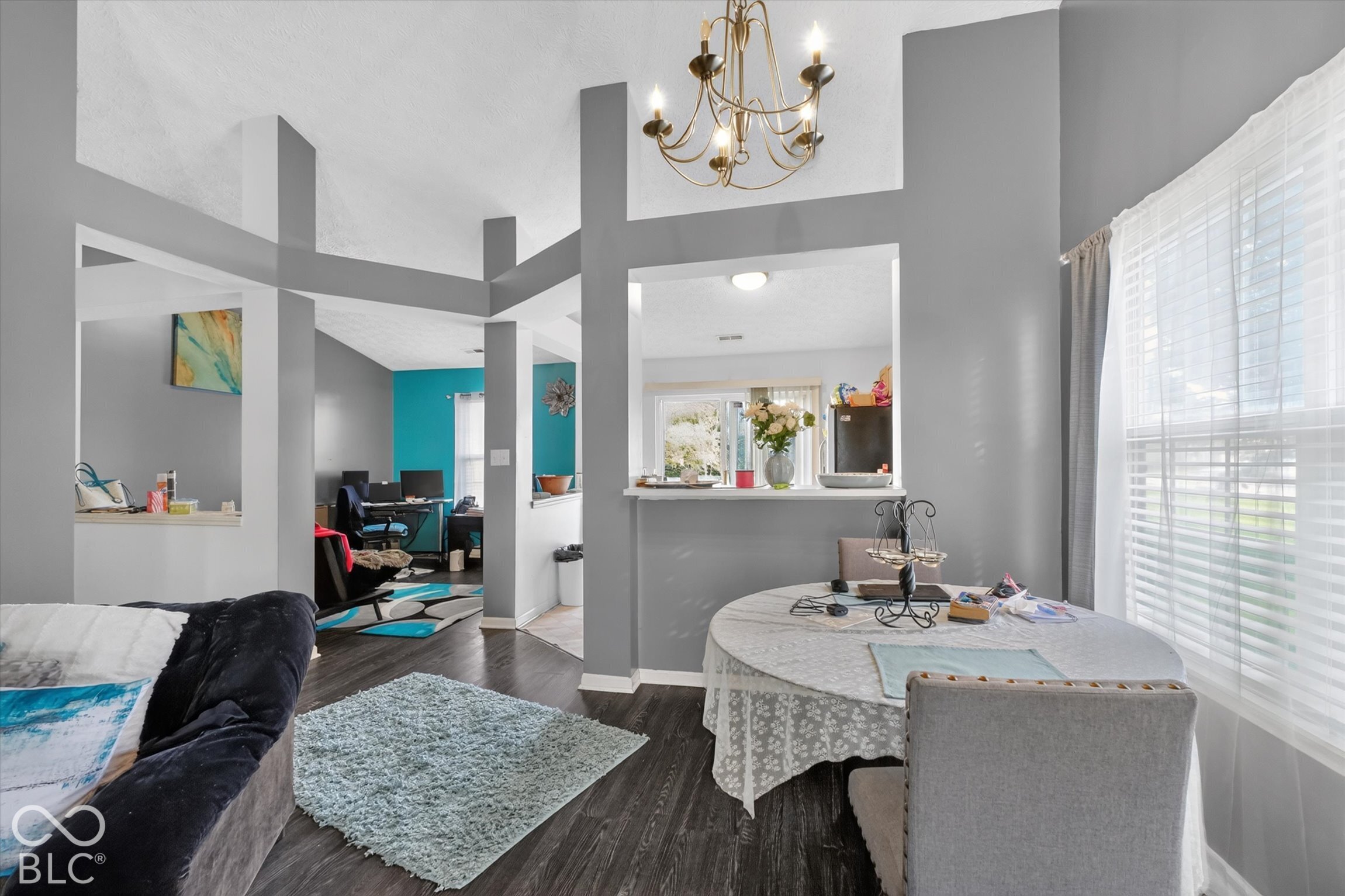 Vaulted ceilings featuring decorative architectural columns, dark wood-finish flooring, a multi-light chandelier, and a breakfast bar pass-through