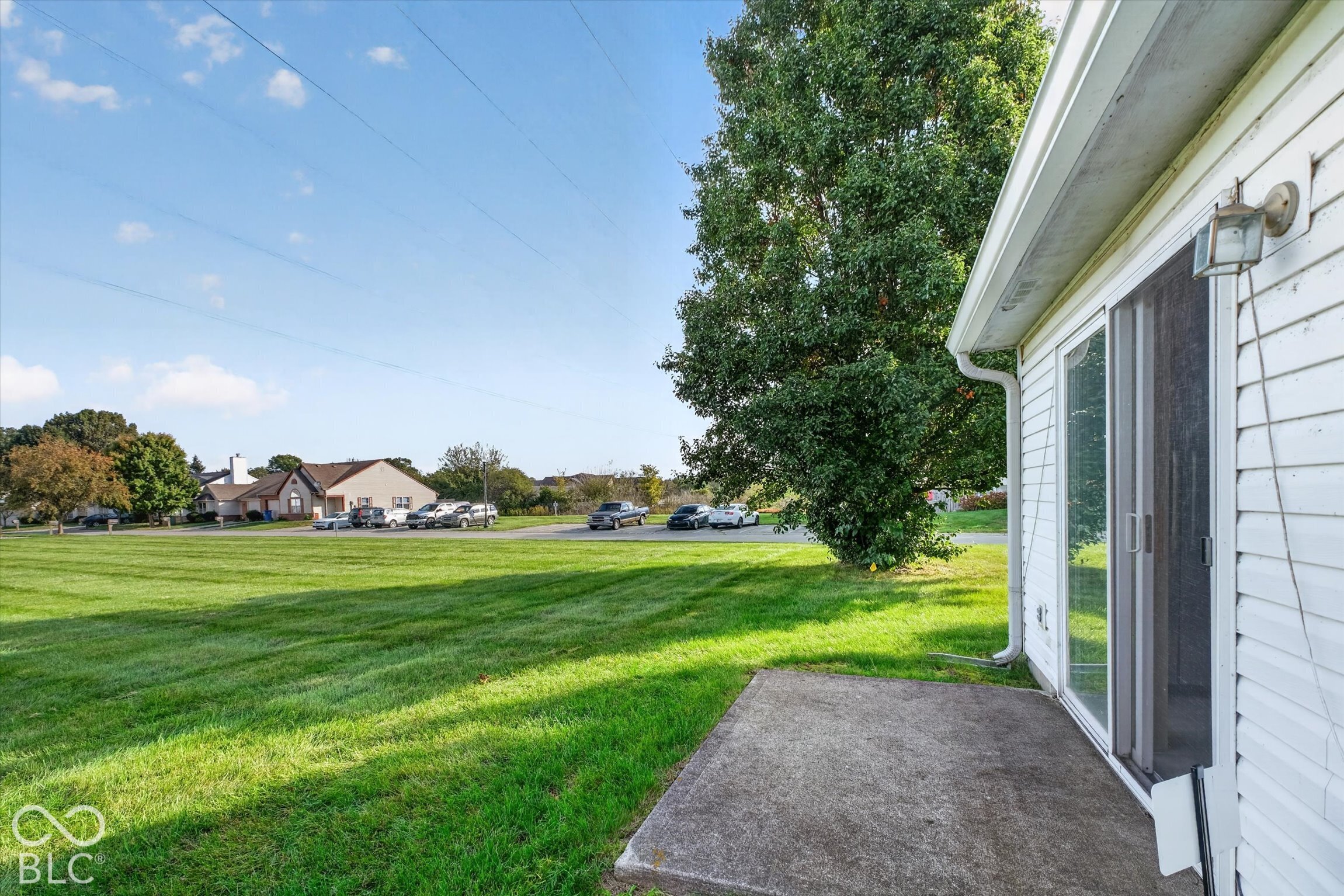 Exterior view featuring white horizontal siding, a concrete patio, sliding glass door, and expansive lawn area