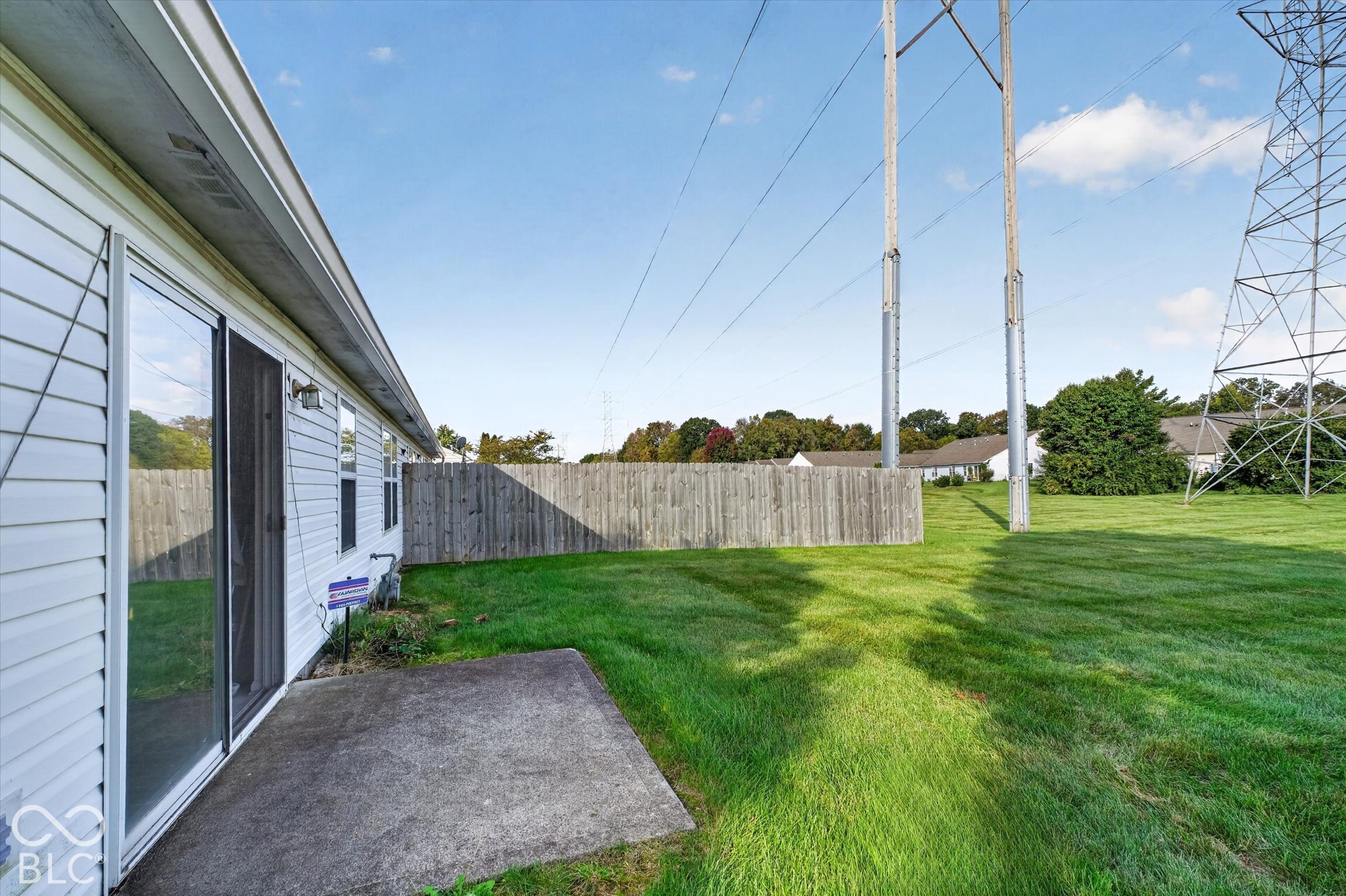 Exterior featuring white horizontal siding, sliding glass patio door, and concrete patio slab within a grass-covered lot enclosed by a wood privacy fence