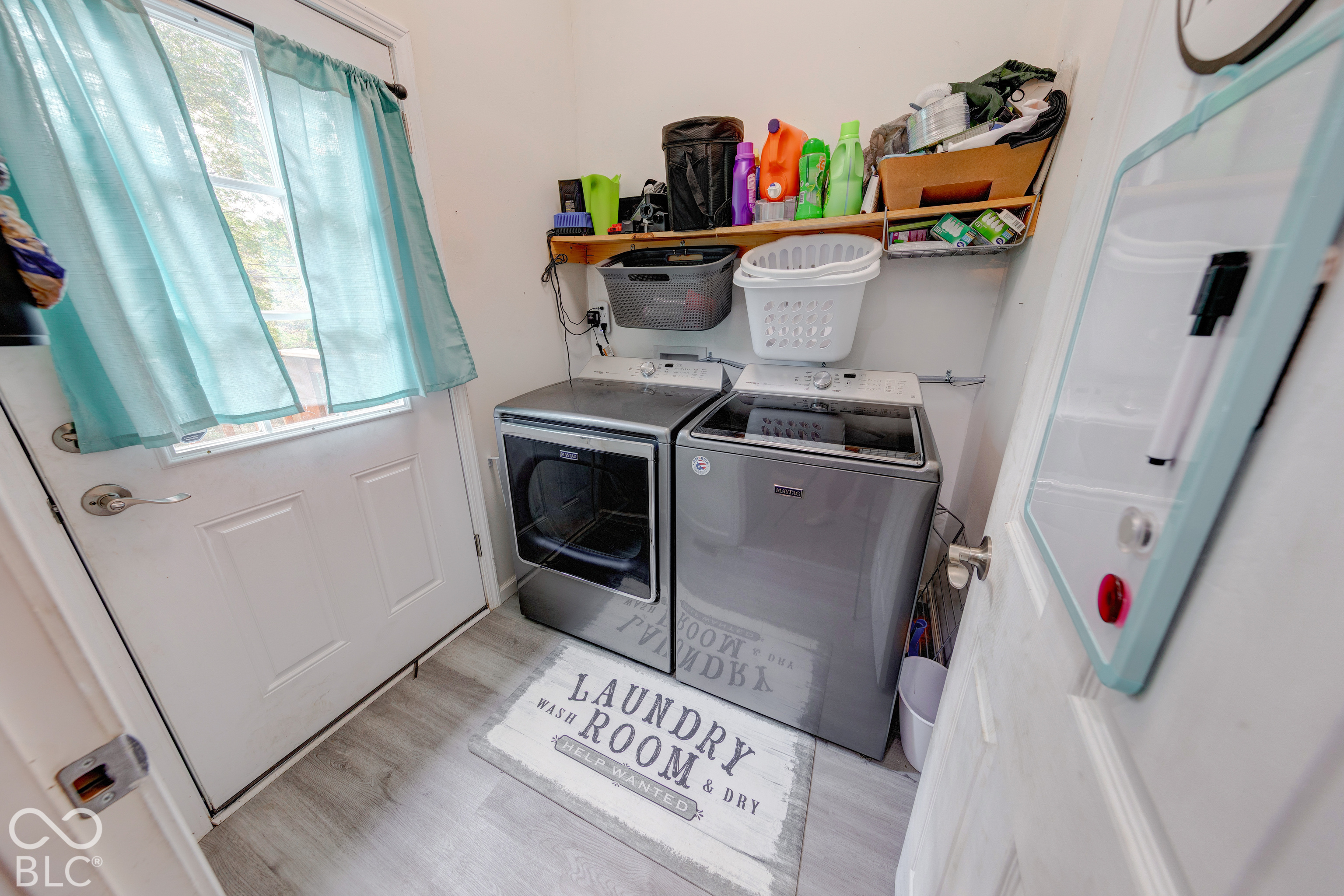 Laundry area featuring wood-finish flooring, a wall-mounted wooden shelf, and a white exterior door with glass insert
