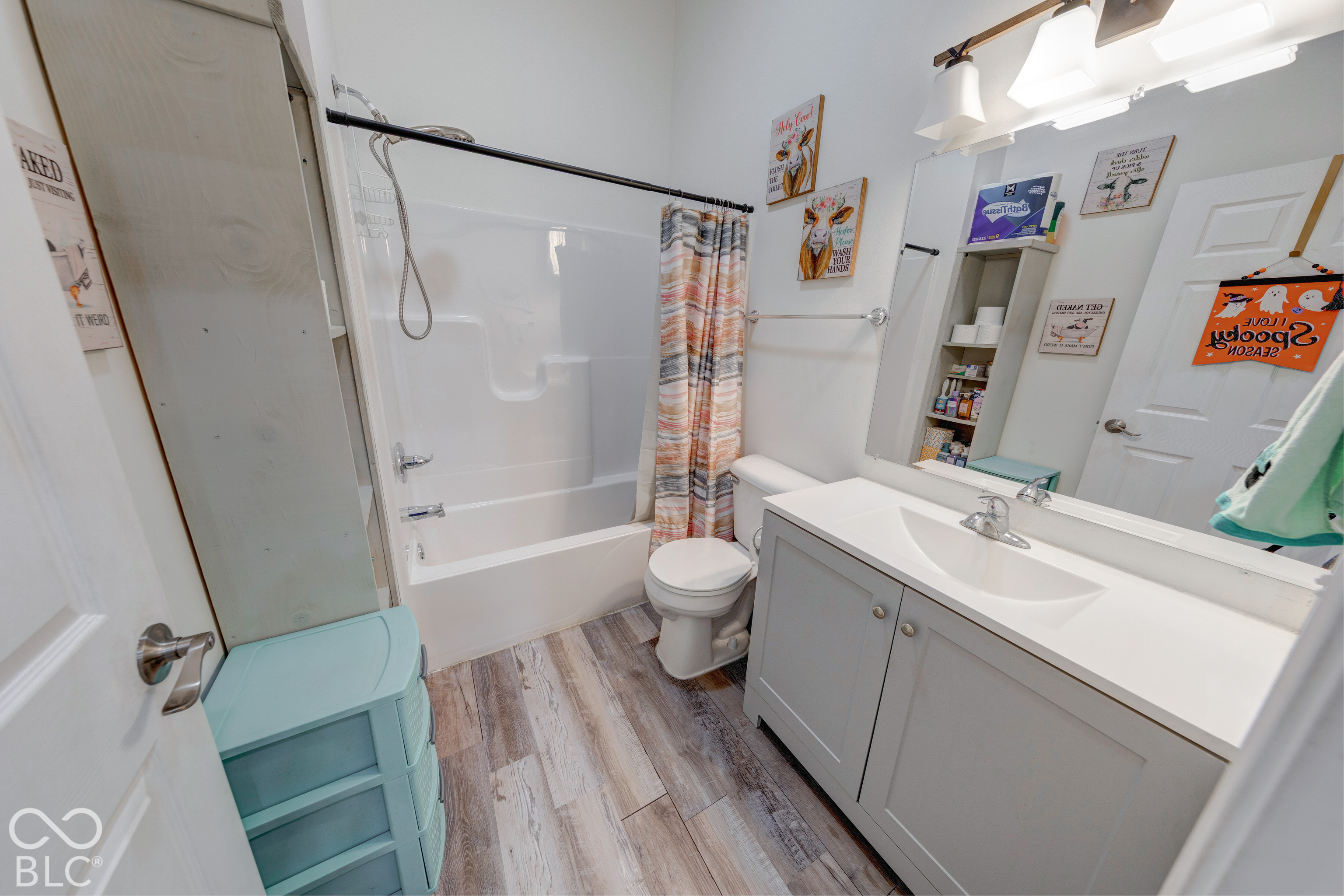 Bathroom featuring wood-finish flooring, a white vanity with integrated sink, a full-wall mirror, polished metal light fixture, and a white tub-shower combination