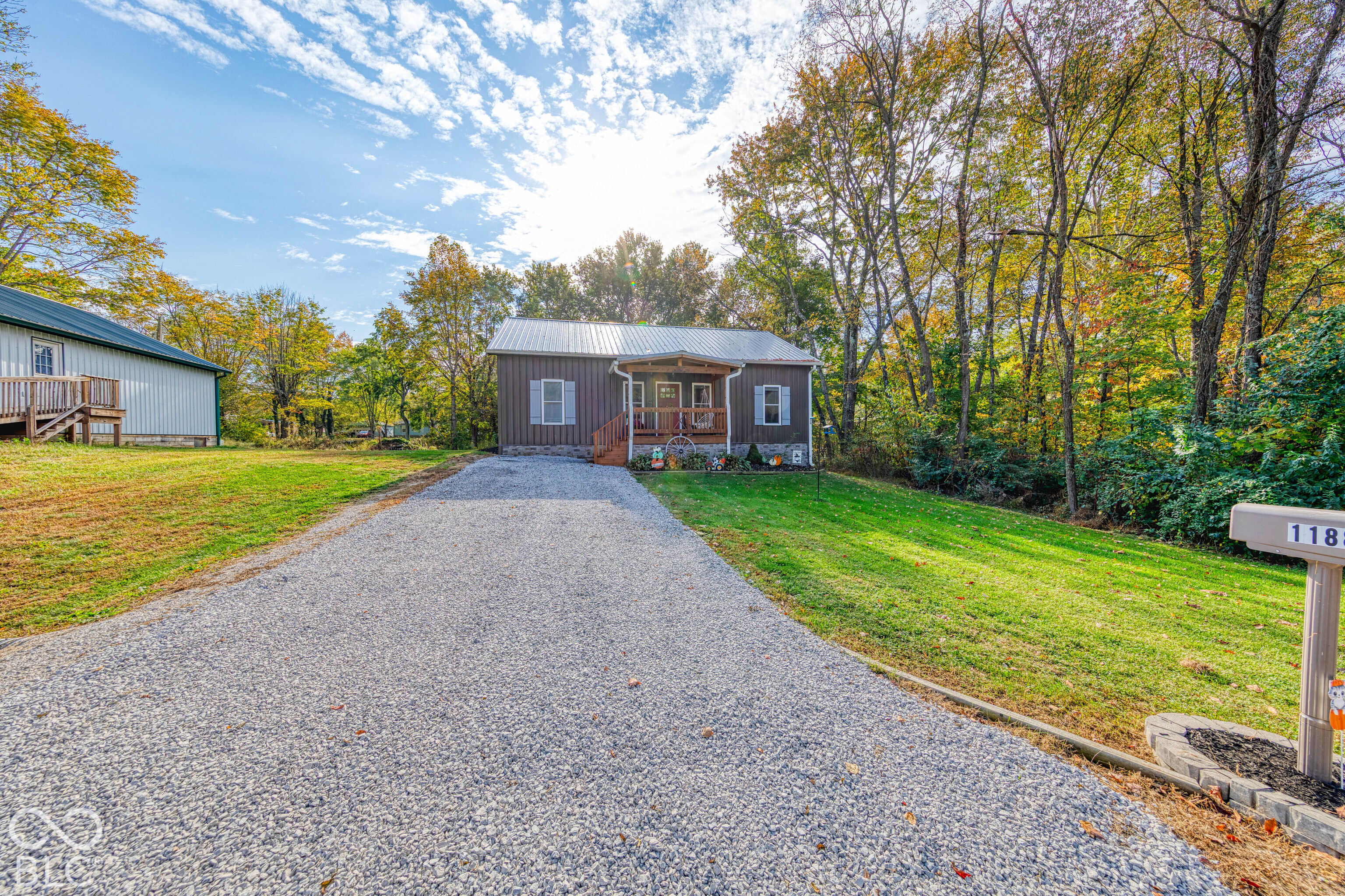 Single-story residence with a metal roof, front covered porch, stone veneer foundation, and a dedicated gravel driveway Single-story residence with a metal roof, front covered porch, stone veneer foundation, and a dedicated gravel driveway