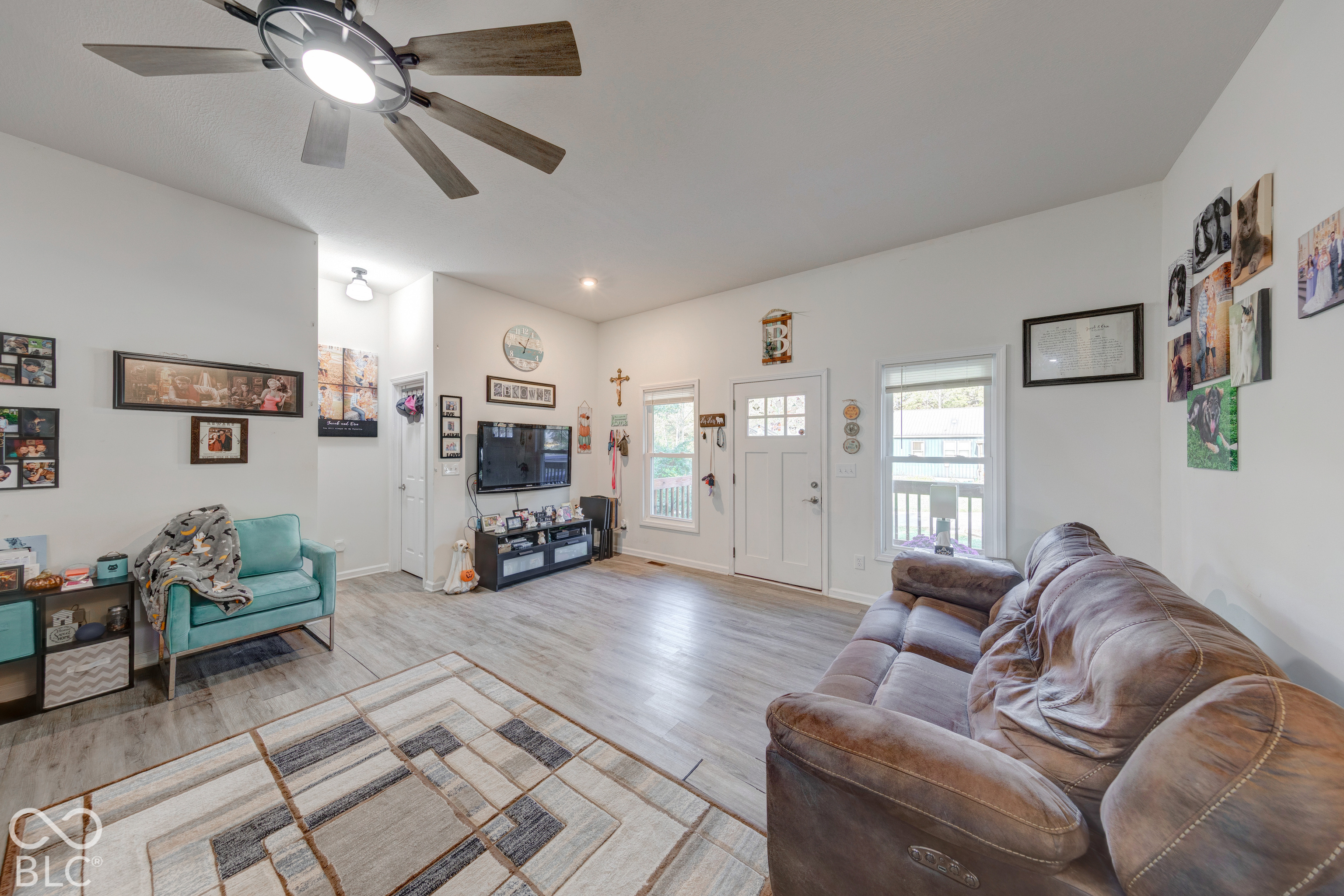 Living area featuring vaulted ceilings, wood-finish flooring, a multi-blade ceiling fan with integrated lighting, and a six-panel glass-inset entry door