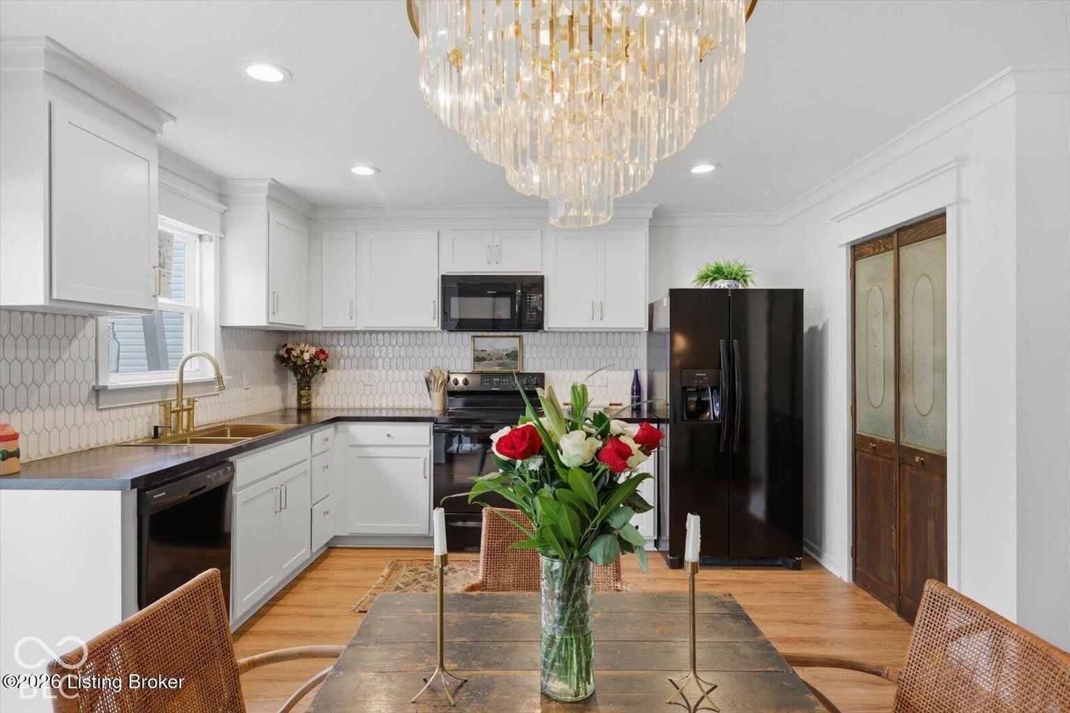 Kitchen featuring white cabinetry, hexagonal tile backsplash, dark countertops, wood-finish flooring, and a crystal chandelier Kitchen featuring white cabinetry, hexagonal tile backsplash, dark countertops, wood-finish flooring, and a crystal chandelier