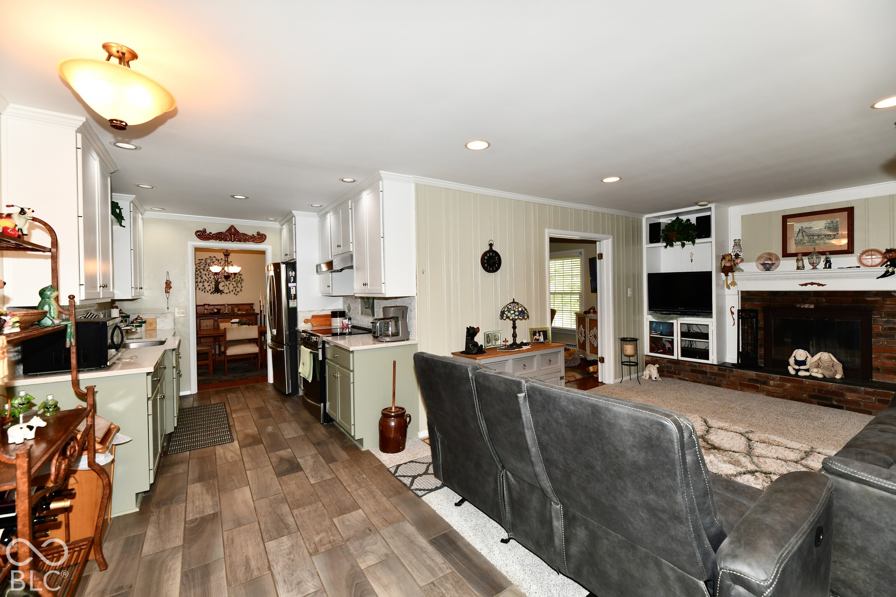 Kitchen featuring light-toned cabinetry, wood-finish flooring, and recessed lighting, paired with a fireplace showcasing a brick surround and built-in shelving