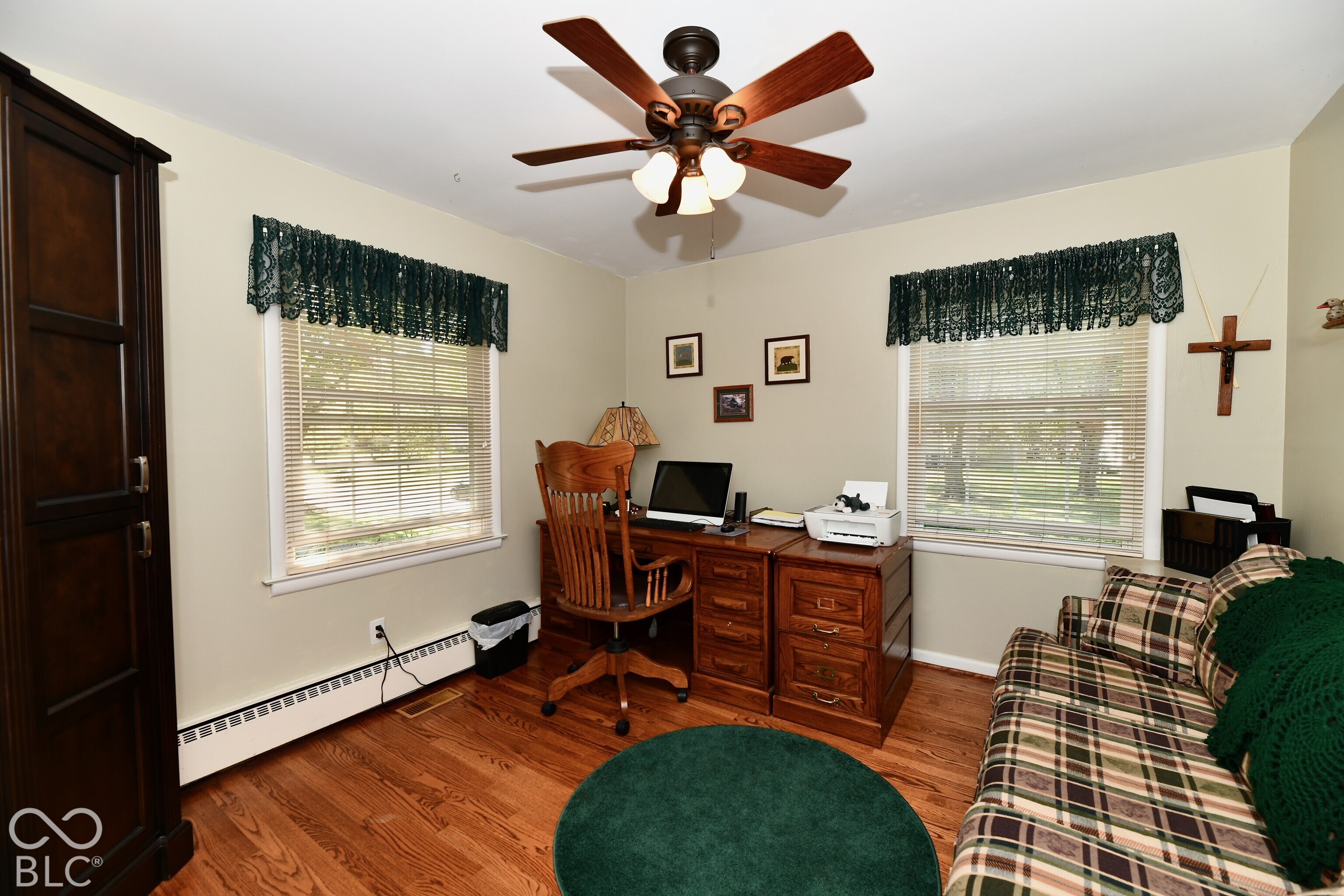 Wood-finish flooring, dual windows with blinds, and a multi-light ceiling fan