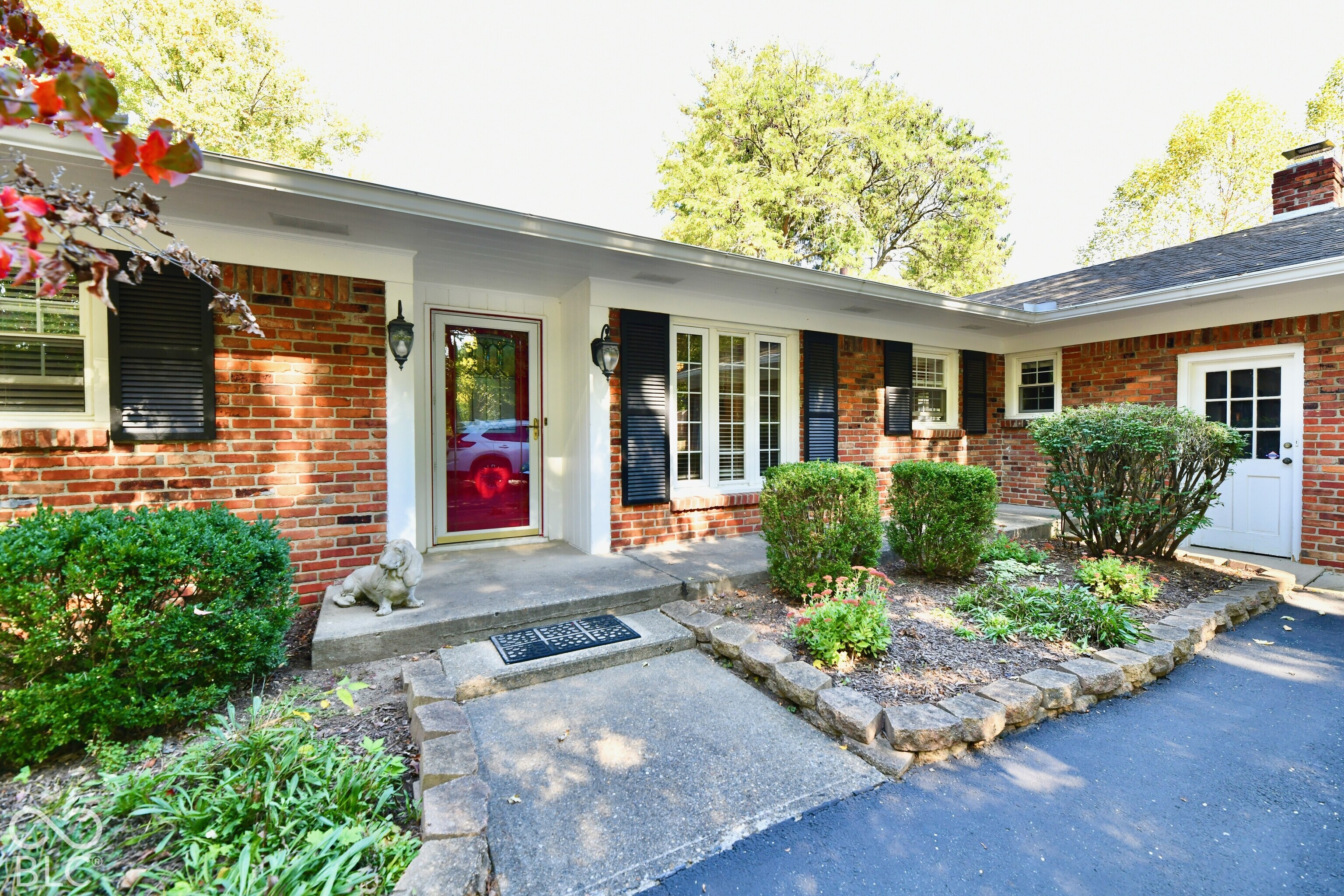 Traditional brick exterior featuring dark shutters, a stone-lined garden bed, concrete walkway, and dual entry points