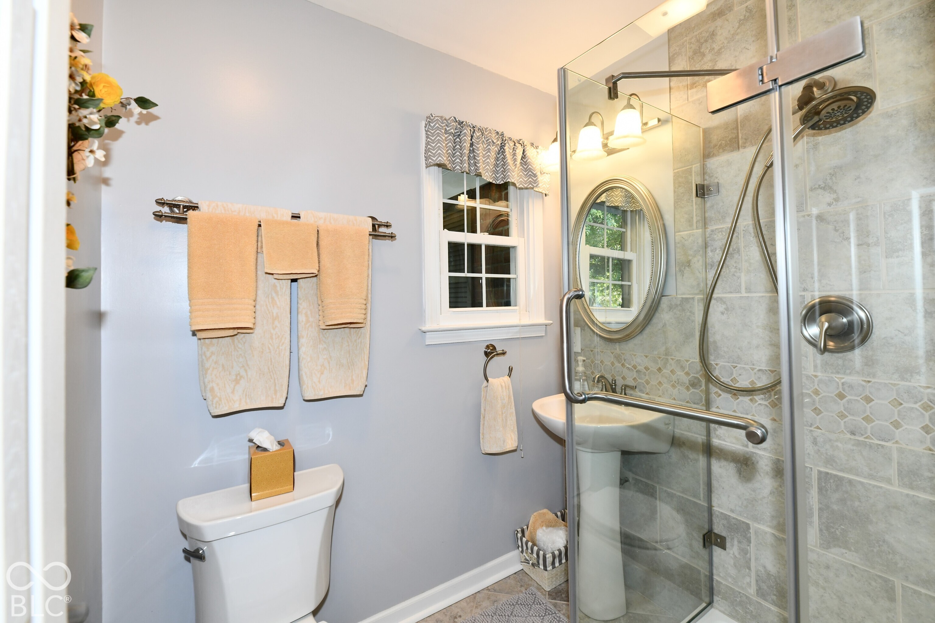 Bathroom featuring a glass-enclosed shower with tiled surround, stone-finish shower walls, pedestal sink, and oval wall-mounted mirror