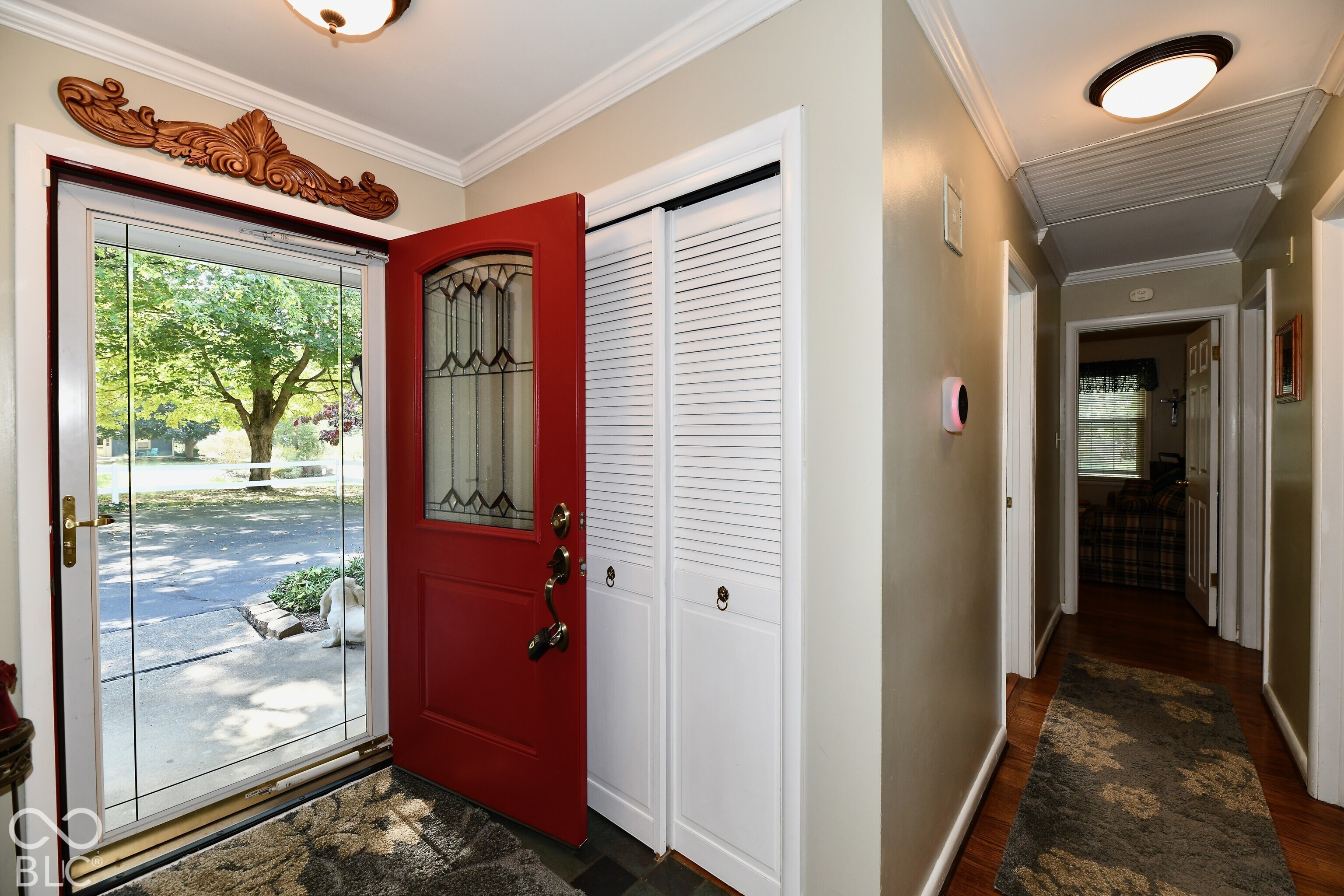 Entryway featuring a solid wood door with a stained-glass insert, louvered bi-fold closet doors, crown molding, and flush-mount ceiling lighting